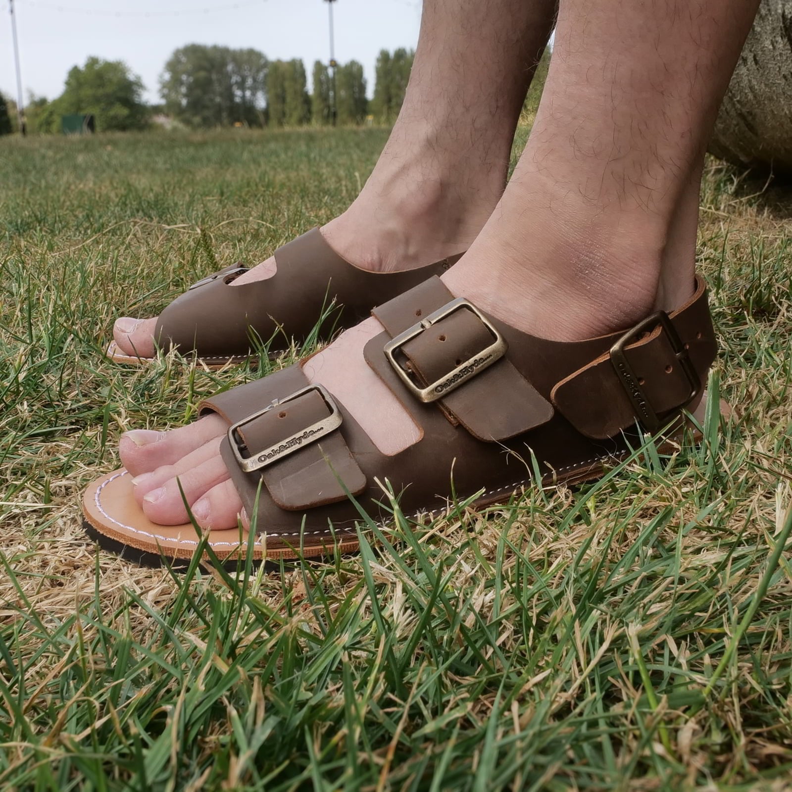 model sitting outdoors wearing mens acacia back strap sandals in brown showing buckles and uppers