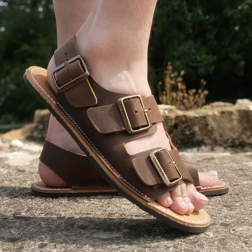 model standing outdoors wearing mens acacia back strap barefoot sandals in brown