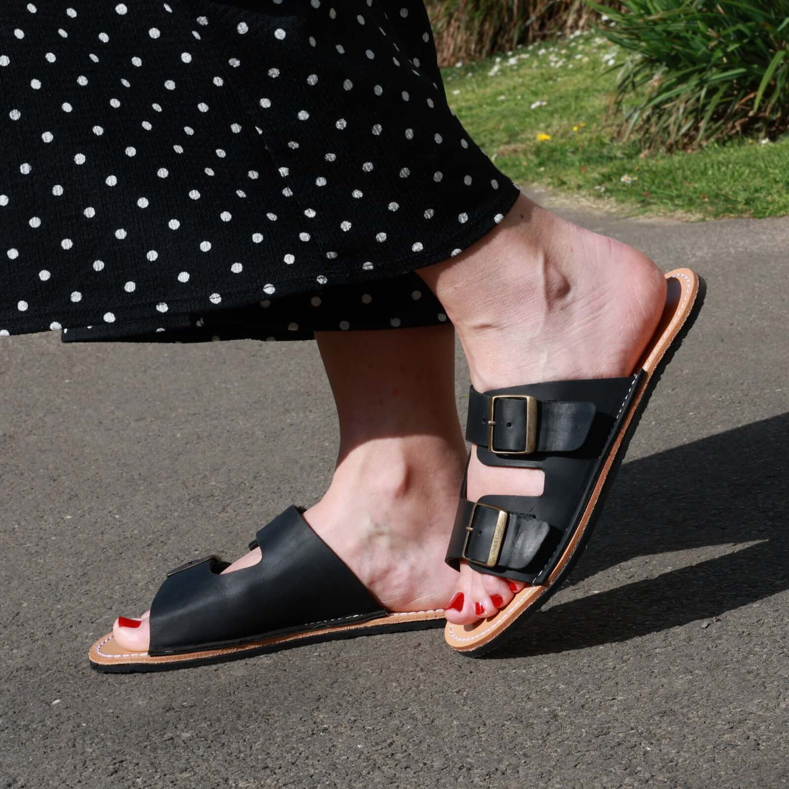 model wearing black acacia barefoot sandals with black spotty trousers on a pavement