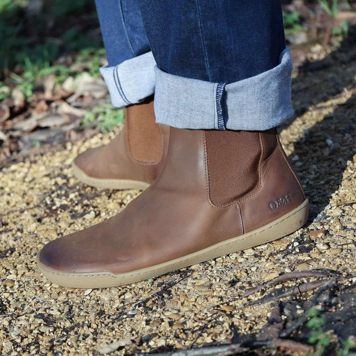 model wearing brown leather barefoot boots with jeans on gravel path outdoors
