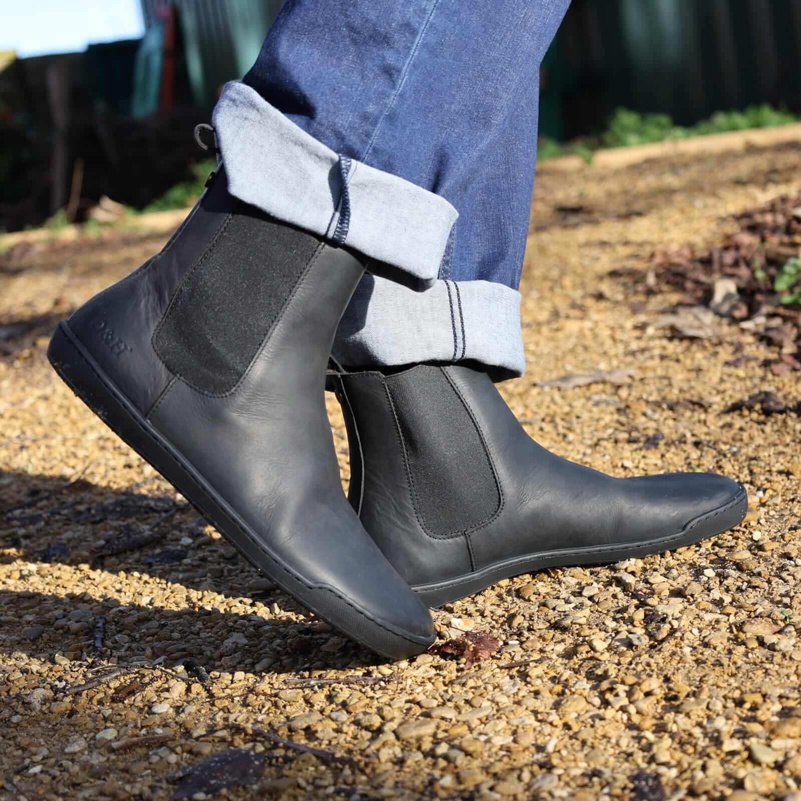 model wearing black barefoot chelsea boots on gravel path outdoors