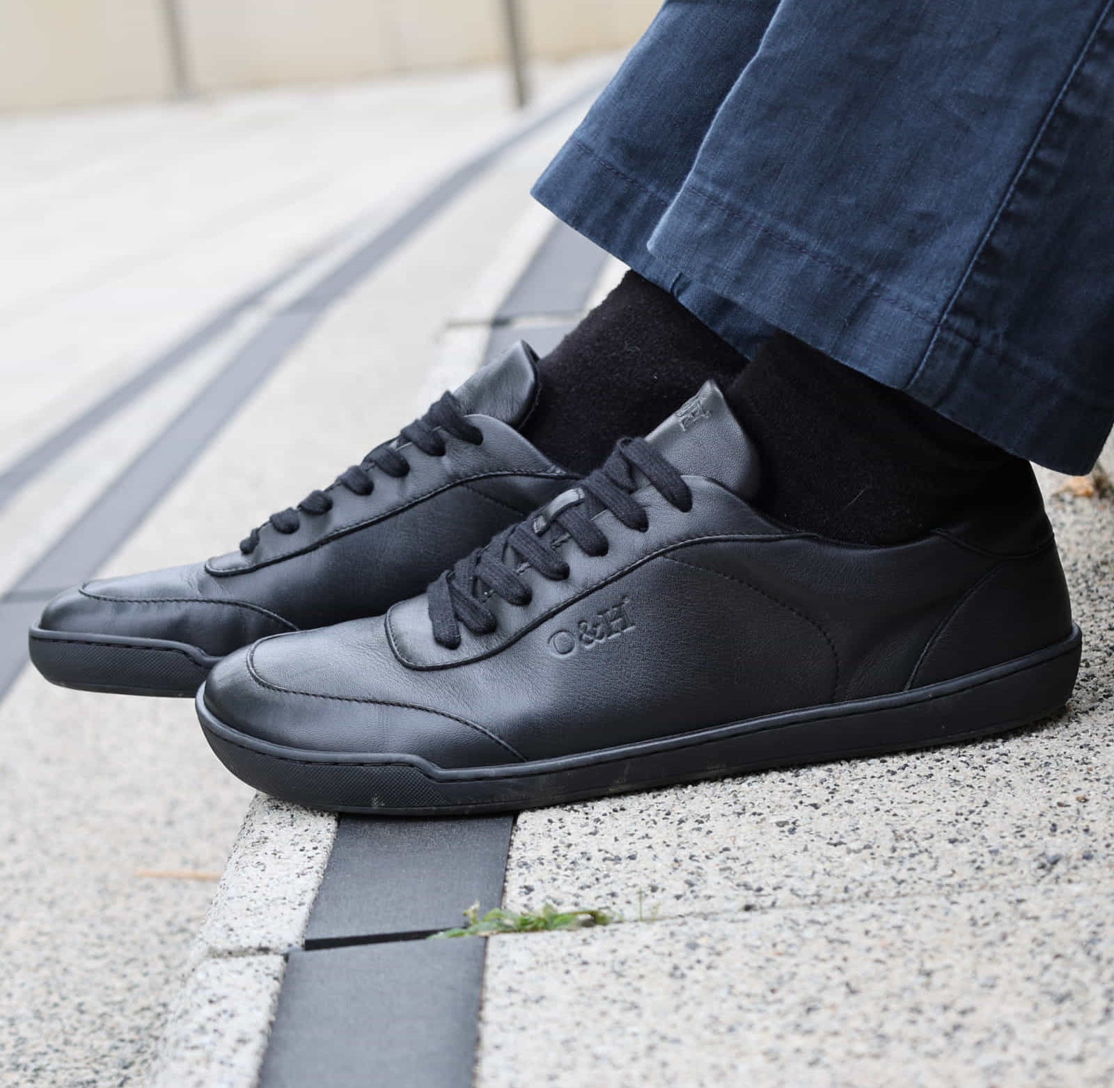 model sitting on steps wearing aspen black barefoot trainers with dark jeans