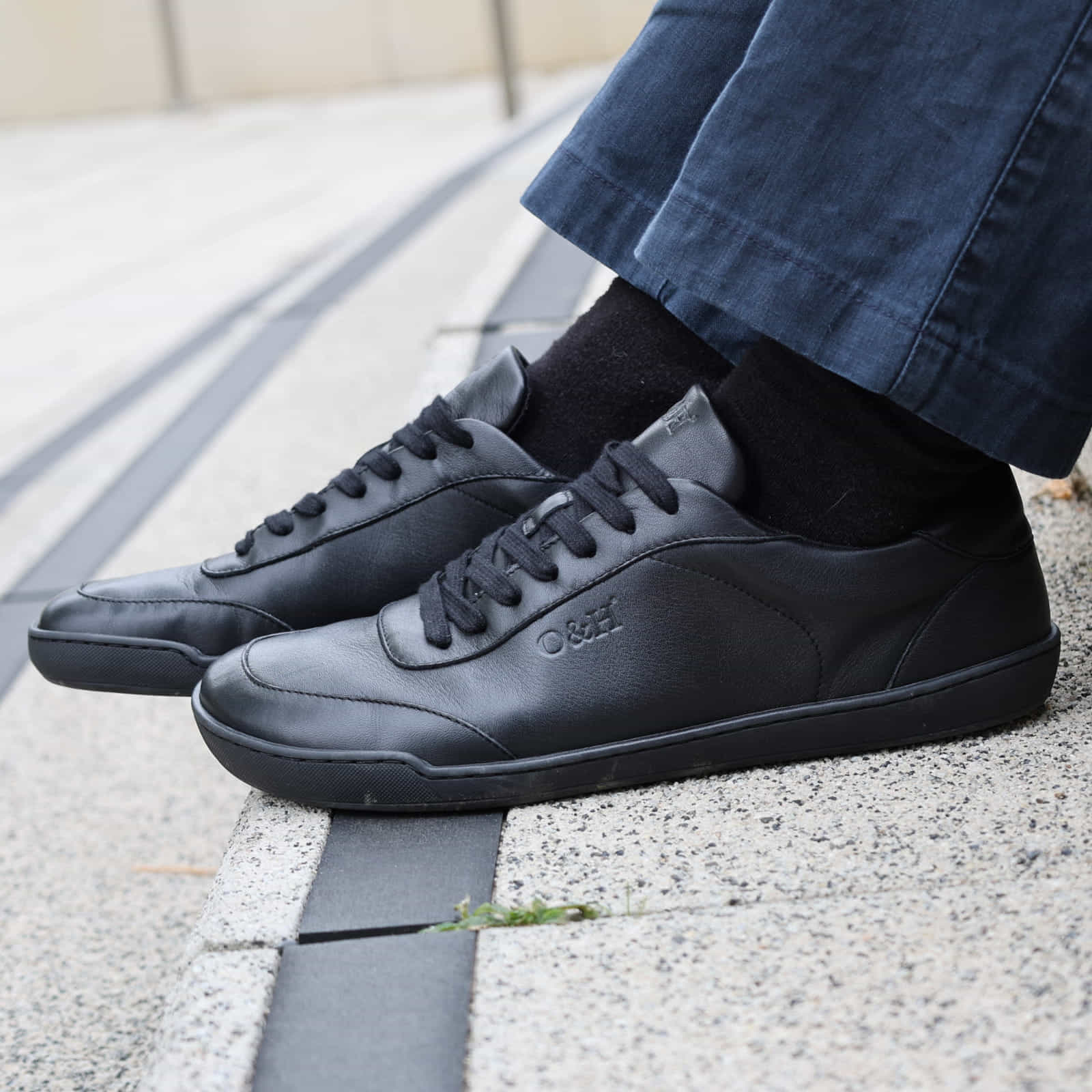 model sitting on steps wearing aspen black barefoot trainers with dark jeans