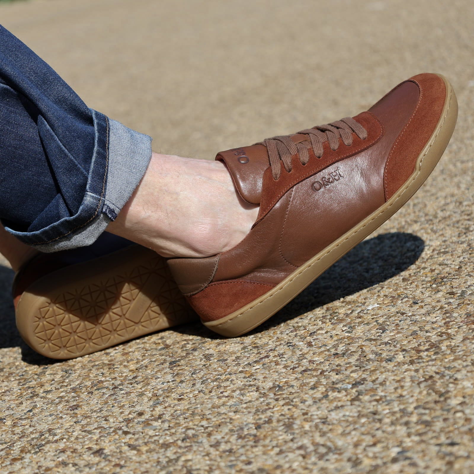 model wearing aspen barefoot trainers in tan with blue jeans sitting on bench