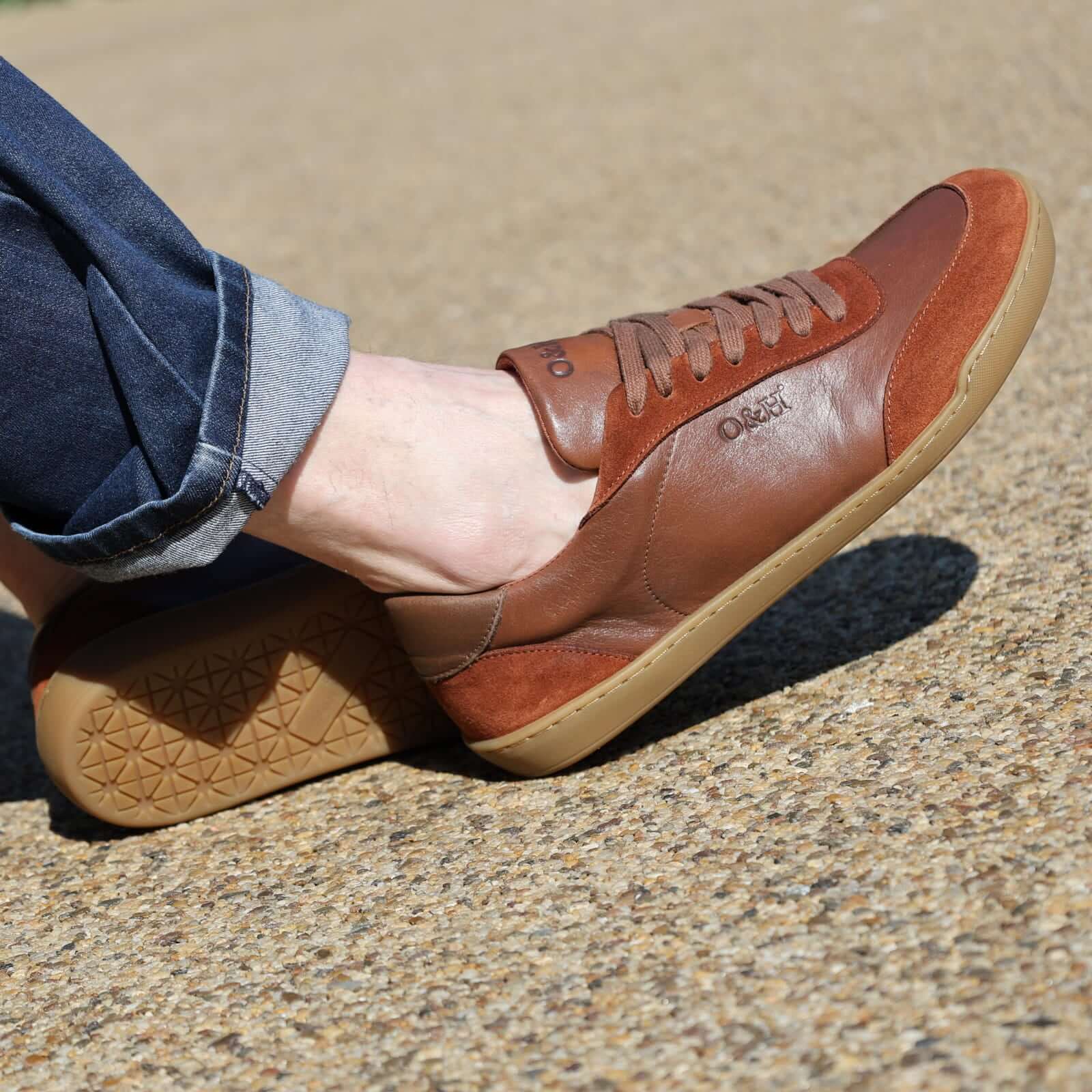model wearing aspen barefoot trainers in tan with blue jeans sitting on bench