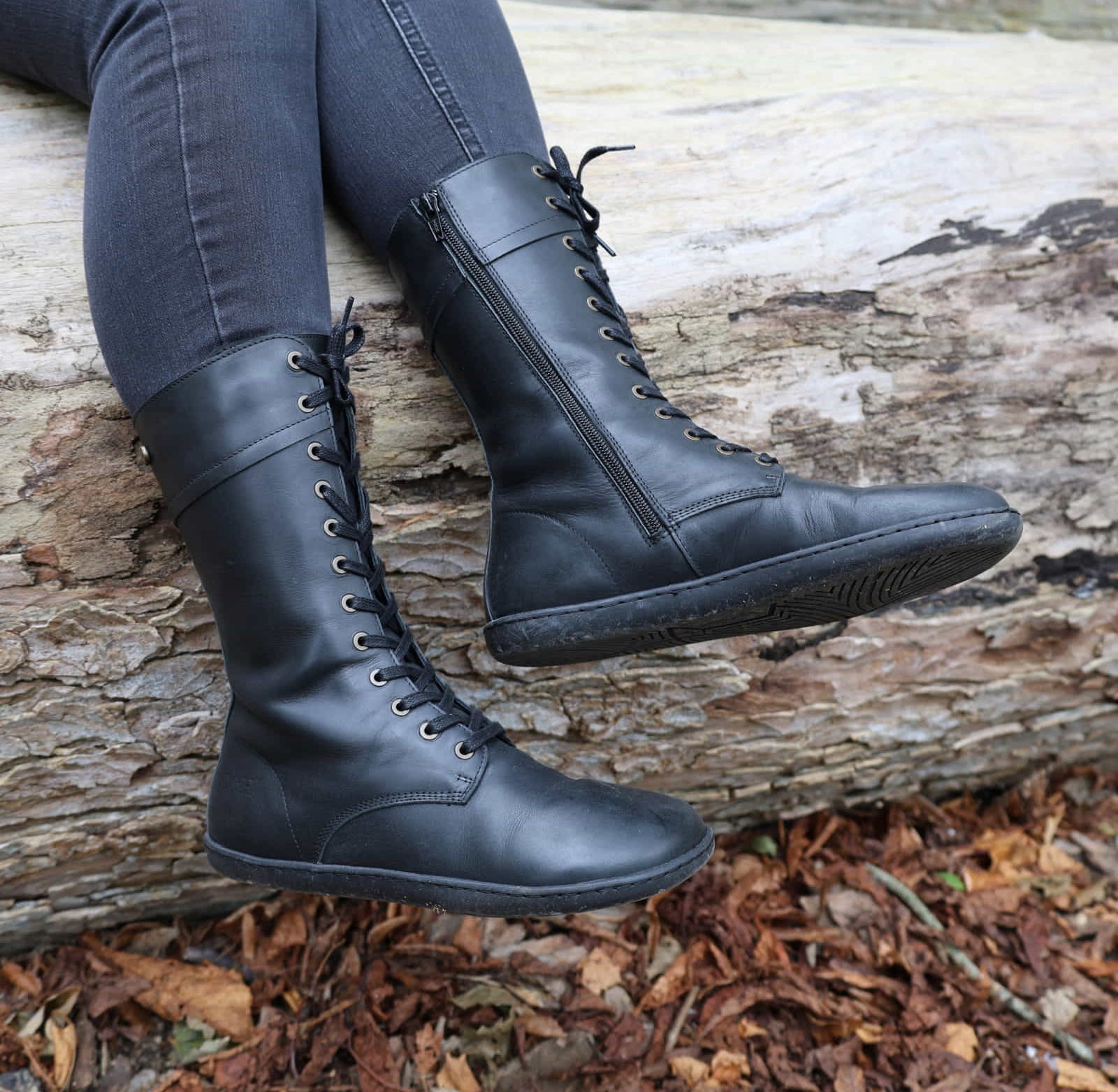 model wearing beech 12 boots in black with jeans sitting on a fallen tree trunk