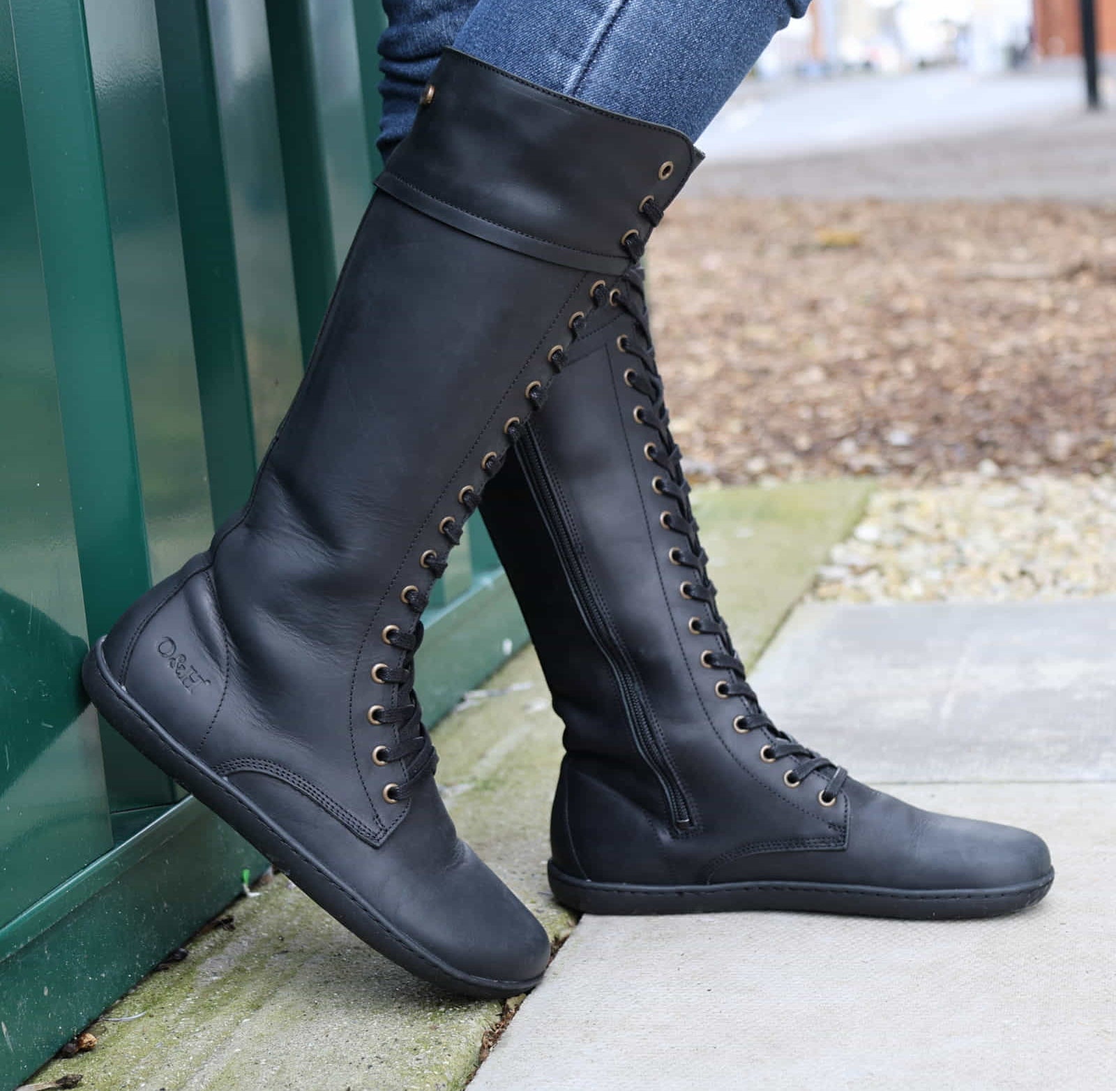person wearing tall black barefoot boots on concrete pavement side on view