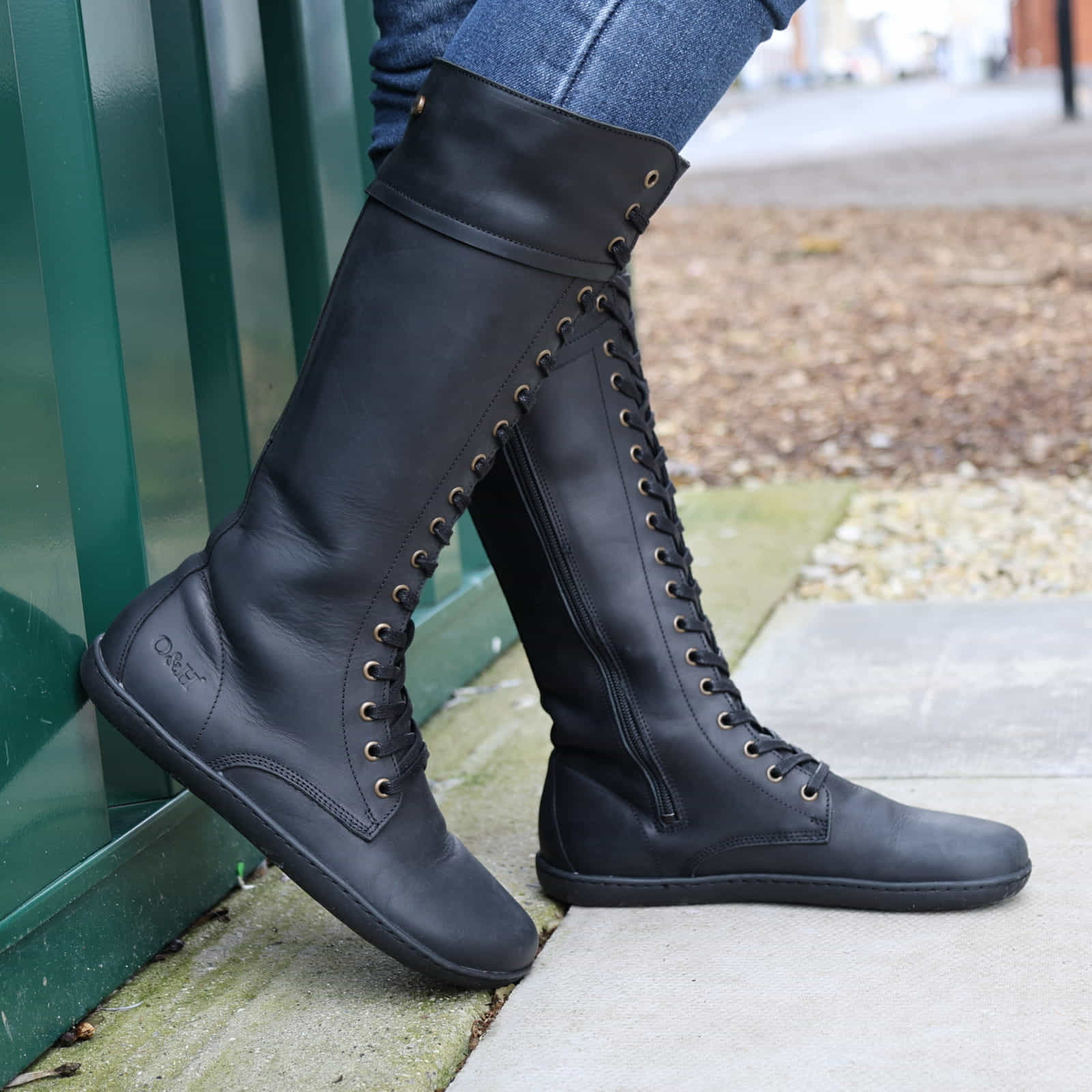 person wearing tall black barefoot boots on concrete pavement side on view