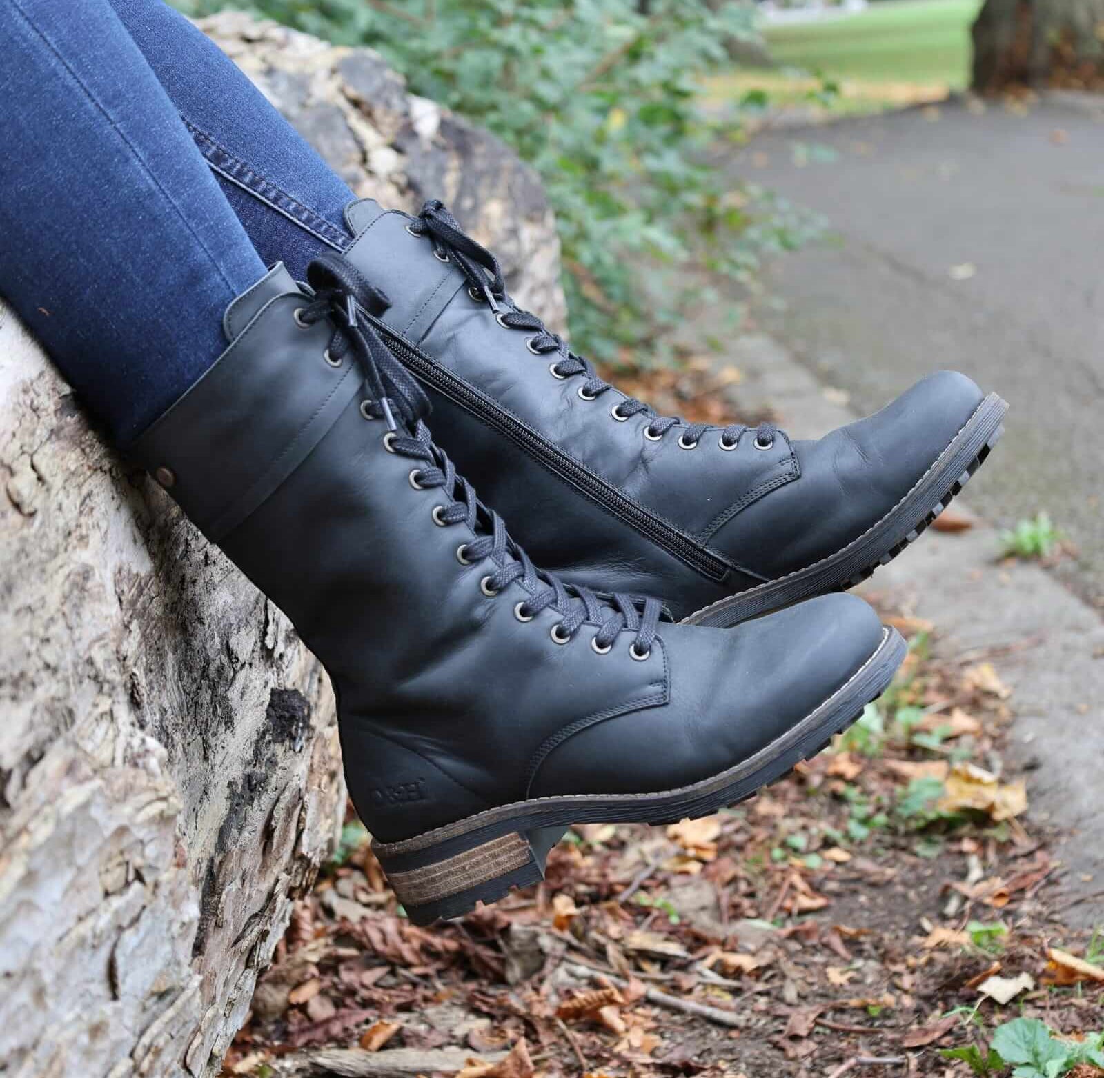 model wearing bridge 12 boots in black sat on a log worn with blue jeans