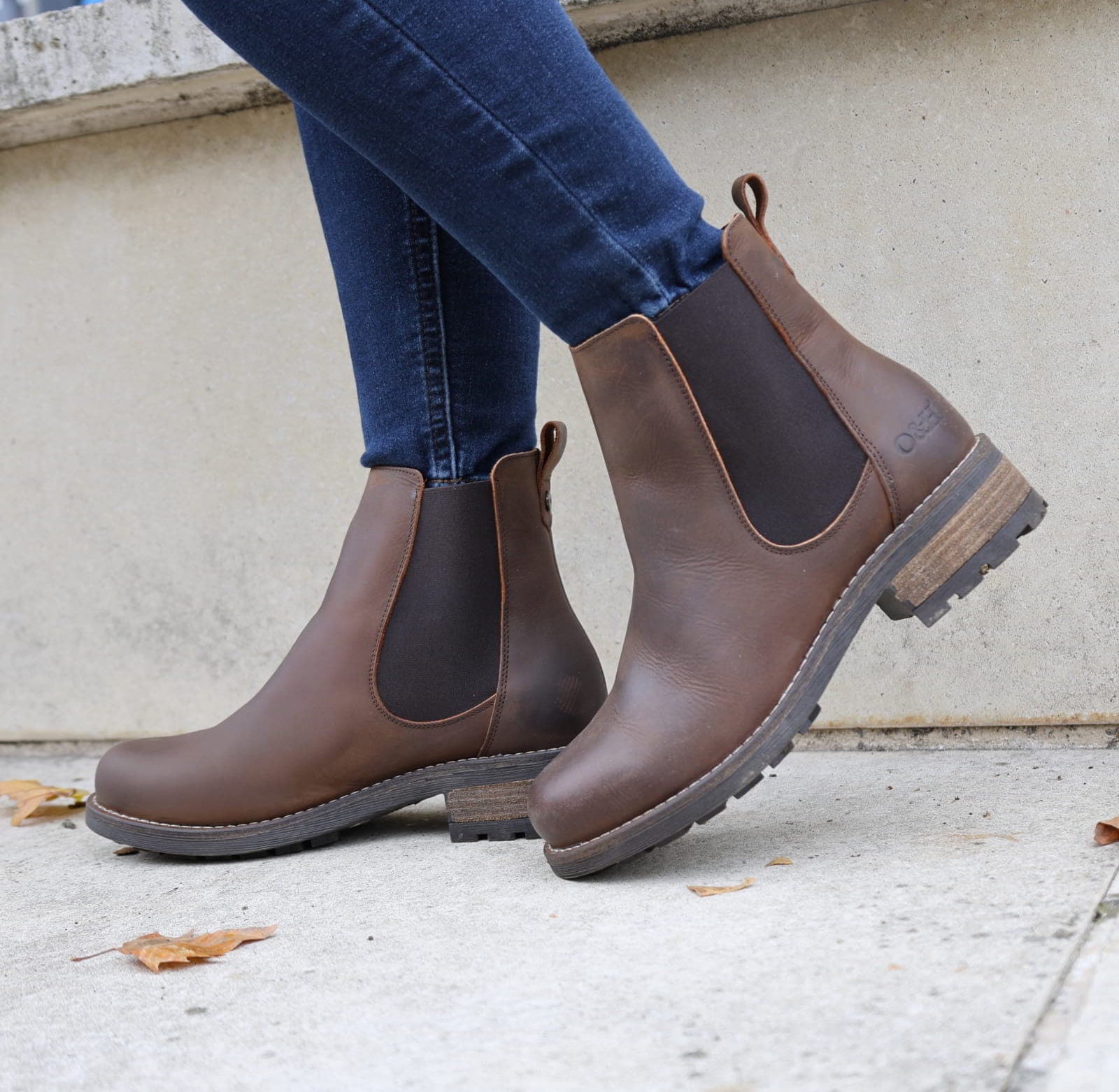 Dark brown Bridge Chelsea 2 boots worn with jeans walking beside a stone wall