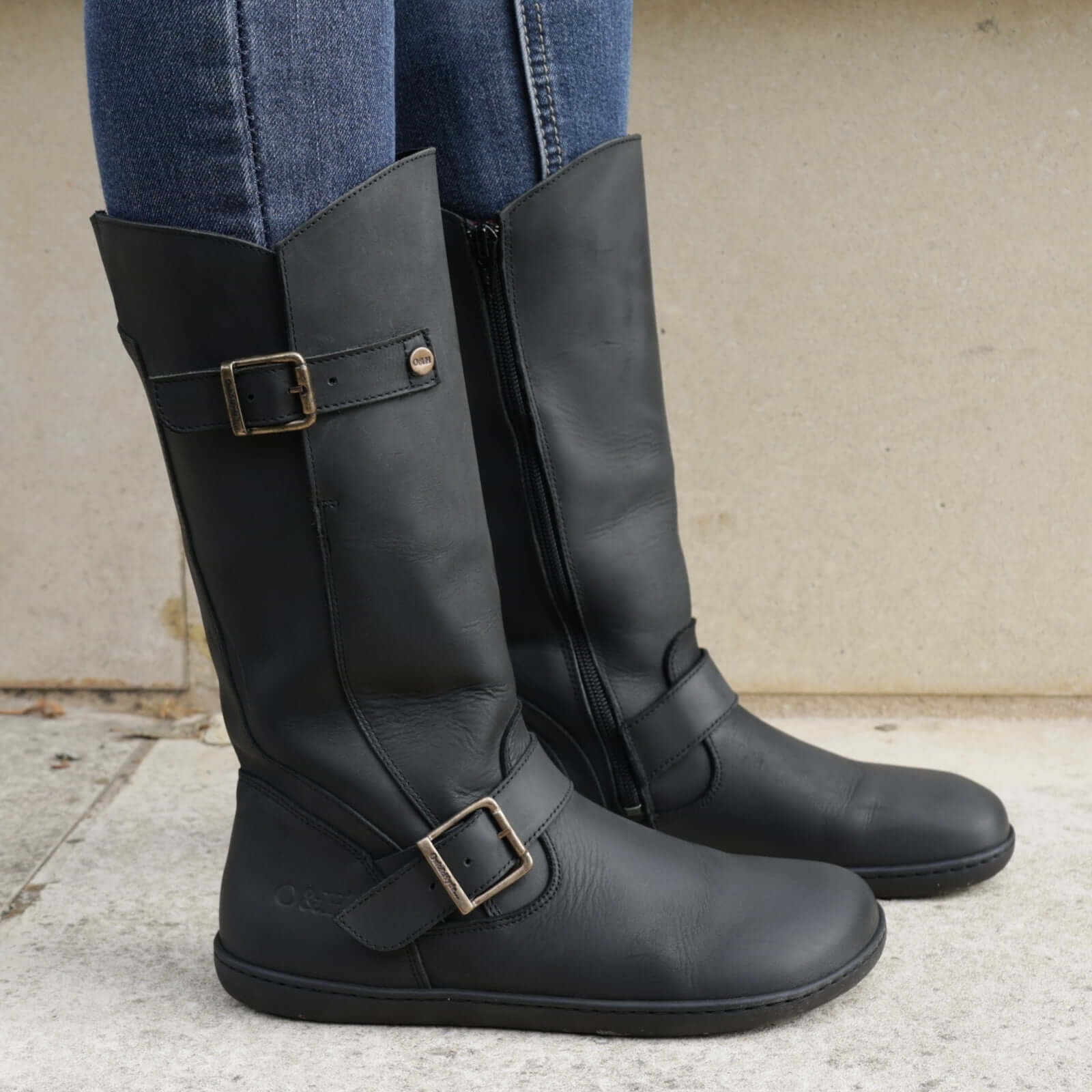 model wearing cedar barefoot boots in black standing on concrete showing buckles
