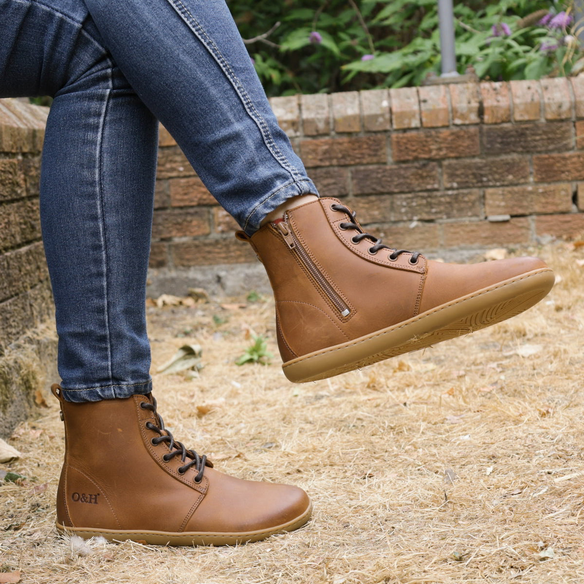 model sitting on wall wearing cherry barefoot ankle boots in cognac with crossed legs