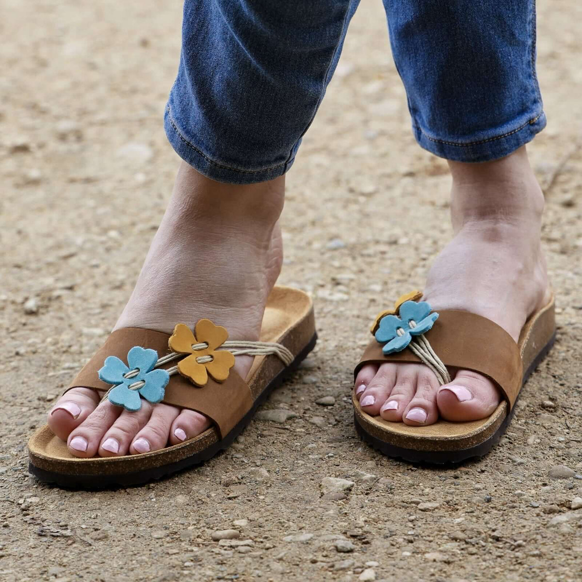 model standing outdoors wearing clover sandals in tan with blue jeans