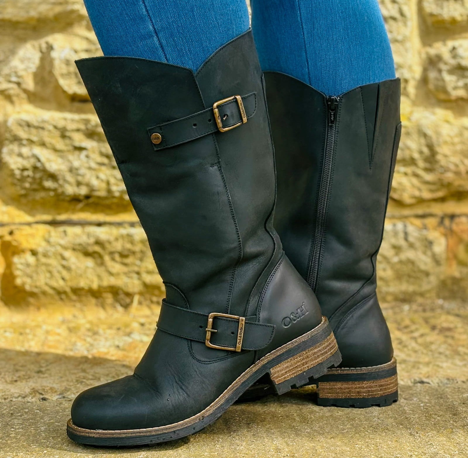 Black Crest 2 wide calf tall boots worn outdoors standing beside a stone wall