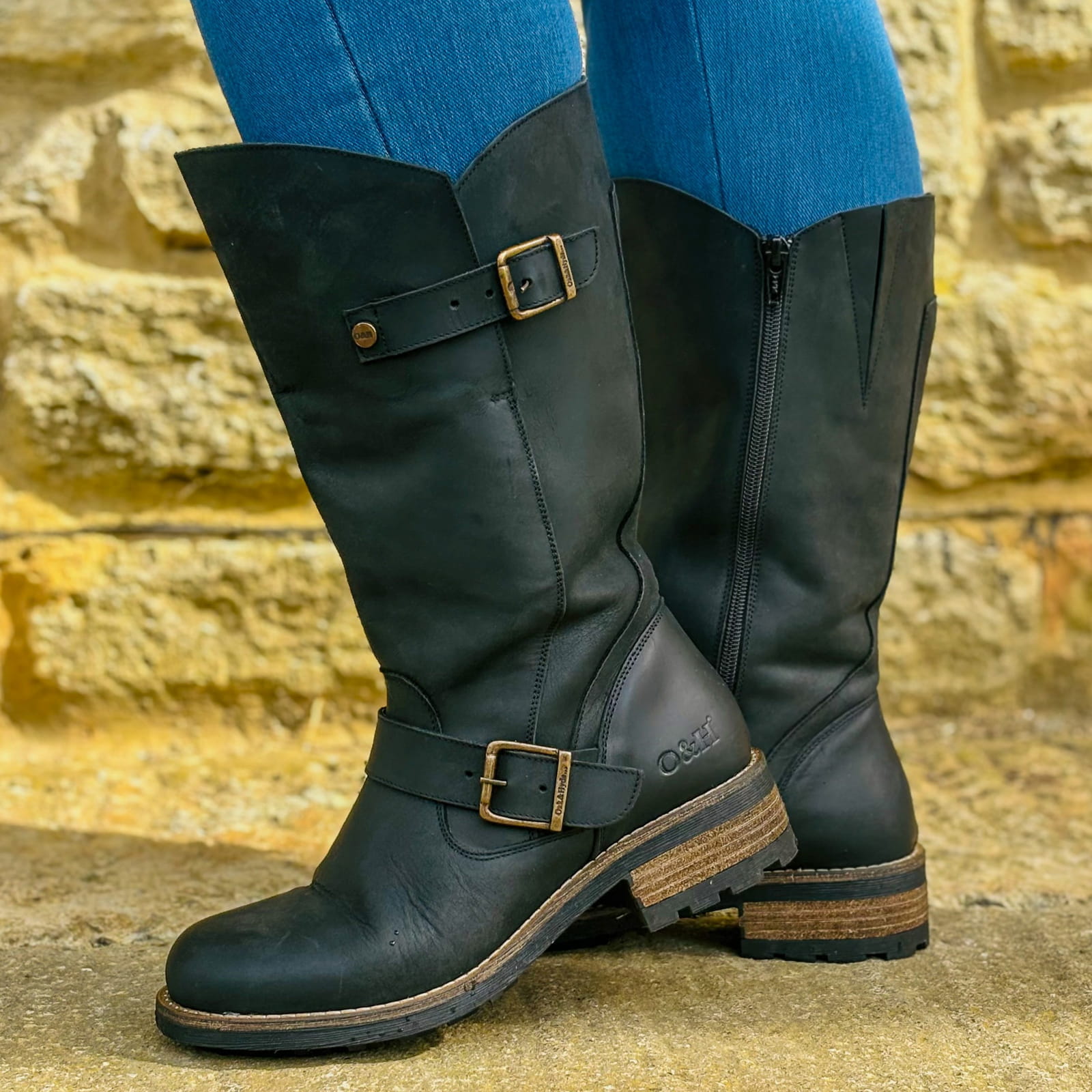 Black Crest 2 wide calf tall boots worn outdoors standing beside a stone wall