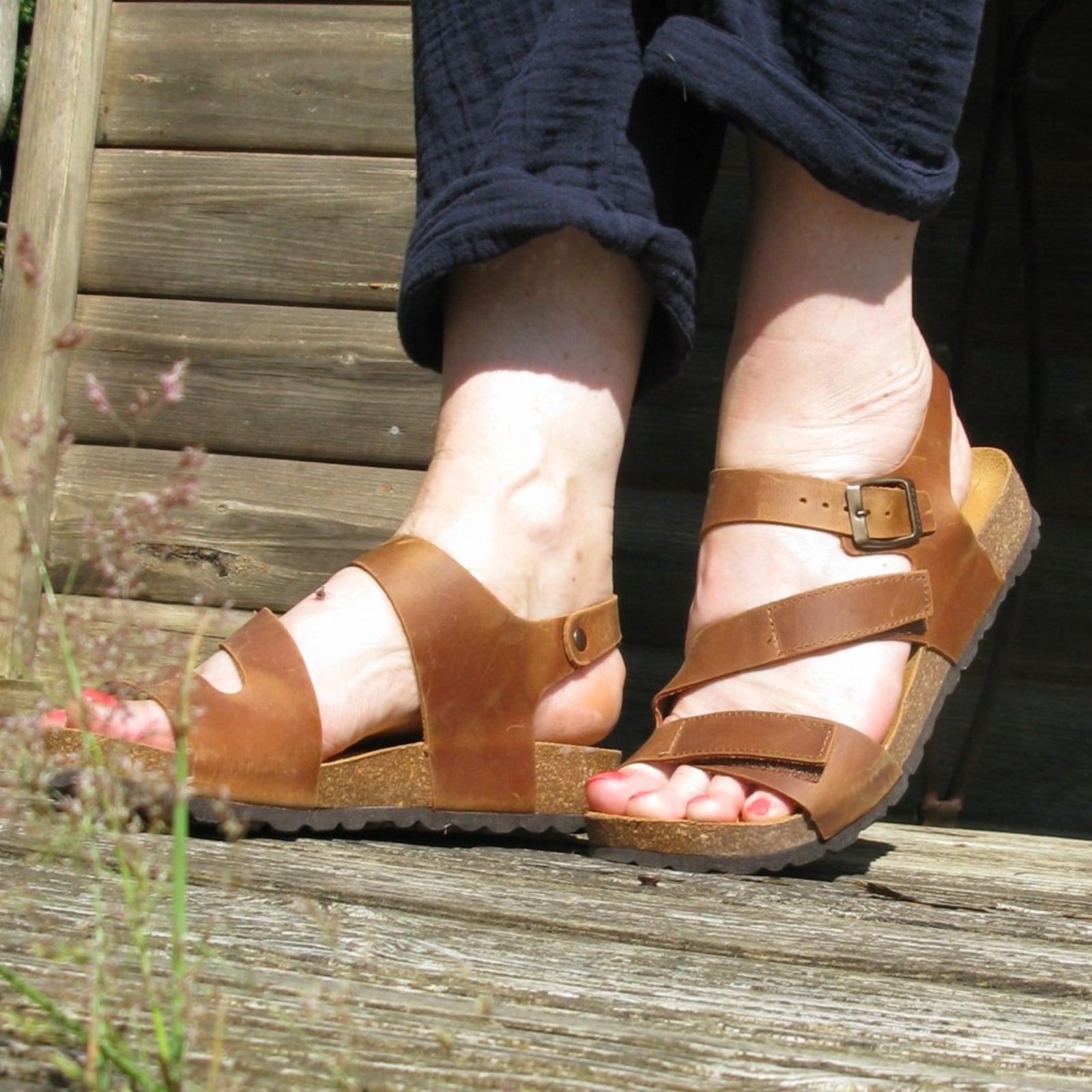 tan oak & hyde daisy sandals worn outdoors on wooden steps with rolled trousers