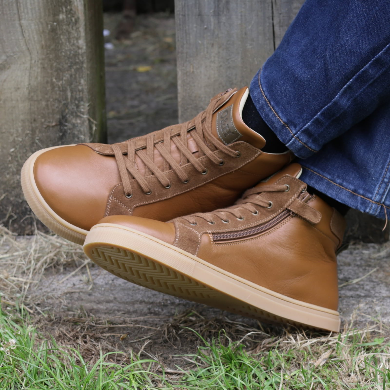 person wearing elm barefoot boots in tan with blue jeans sitting cross legged on a bench