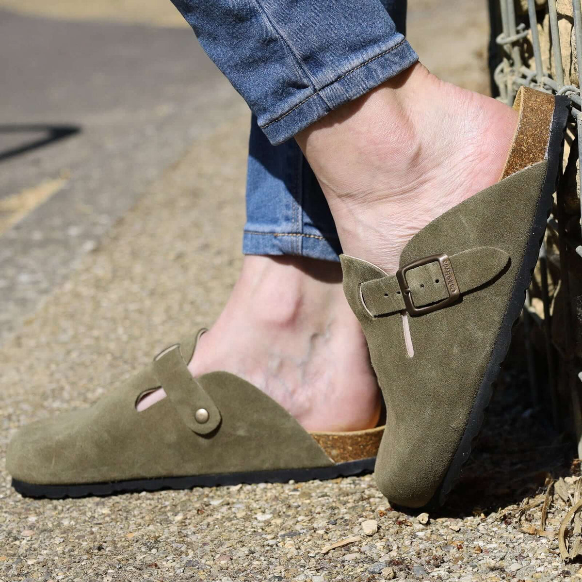 model wearing green leather clogs with jeans leaning against a stone wall