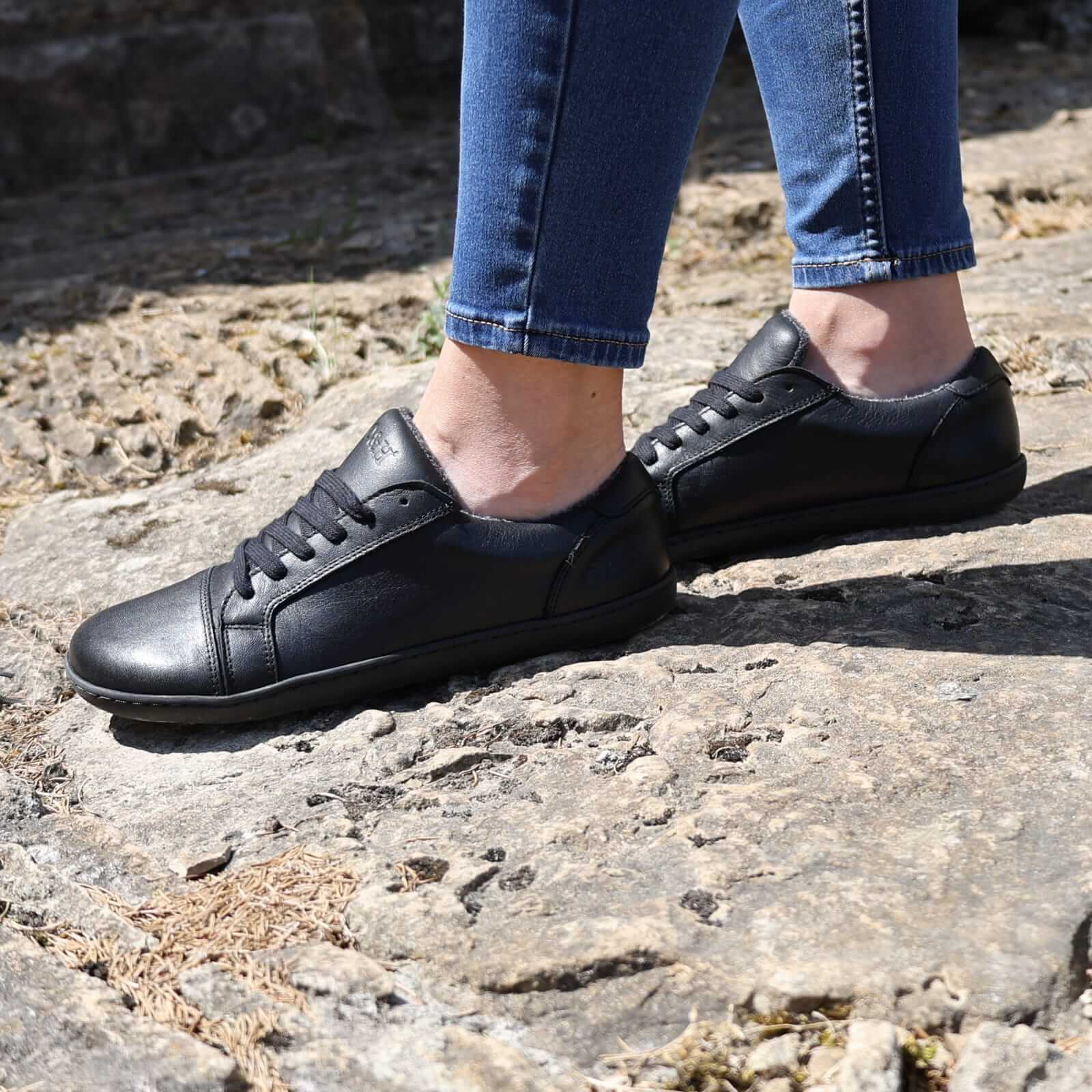 model standing on stone path wearing black barefoot trainers with blue jeans