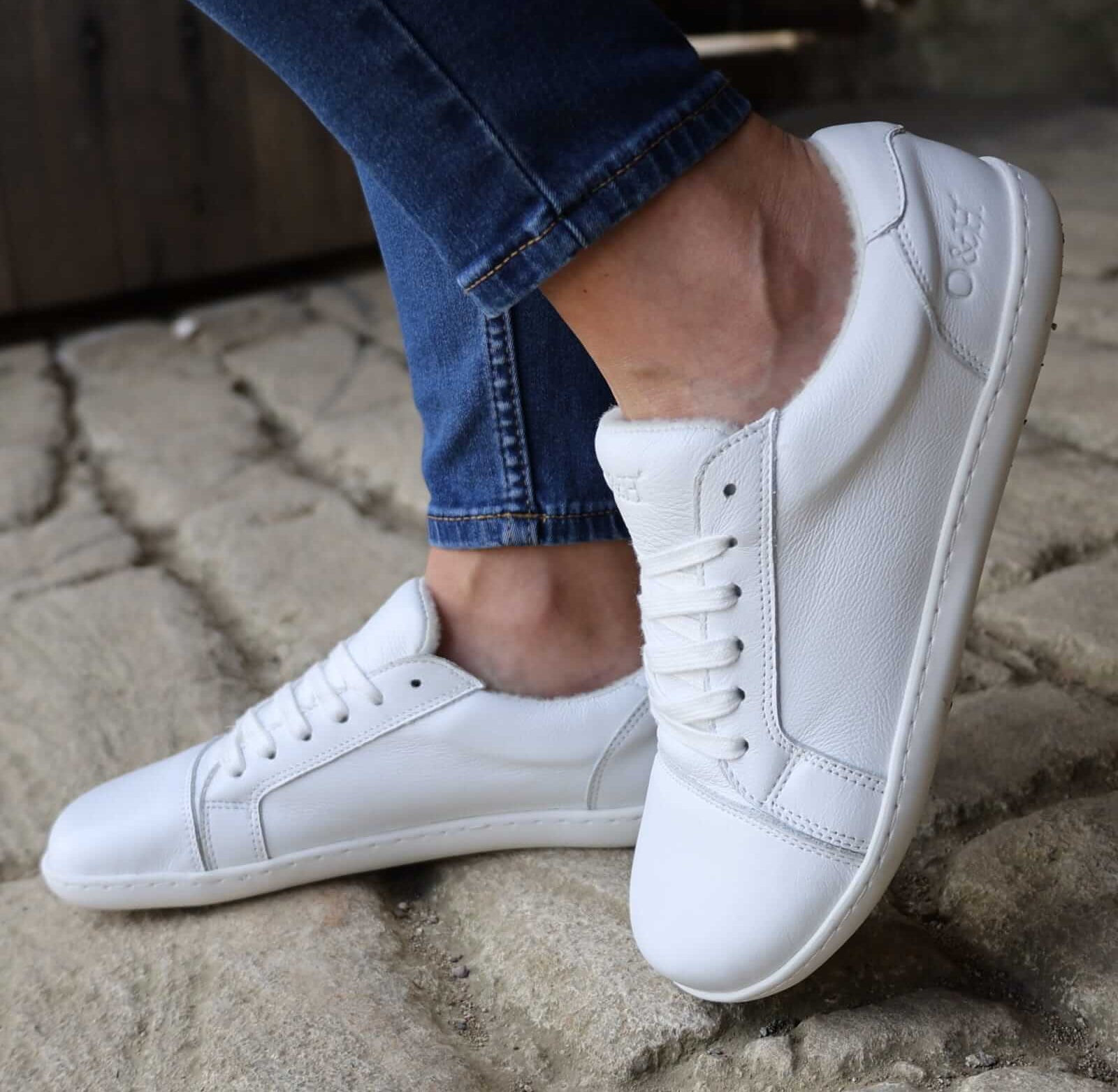 model wearing white trainers with blue jeans standing on stone pavement