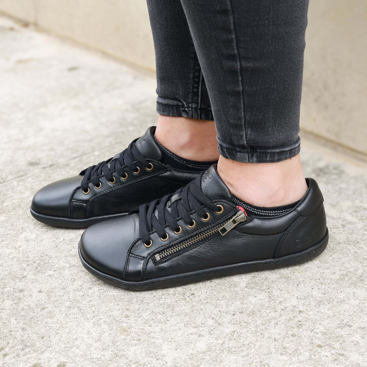 Model wearing hazel zip trainers in black standing on concrete path
