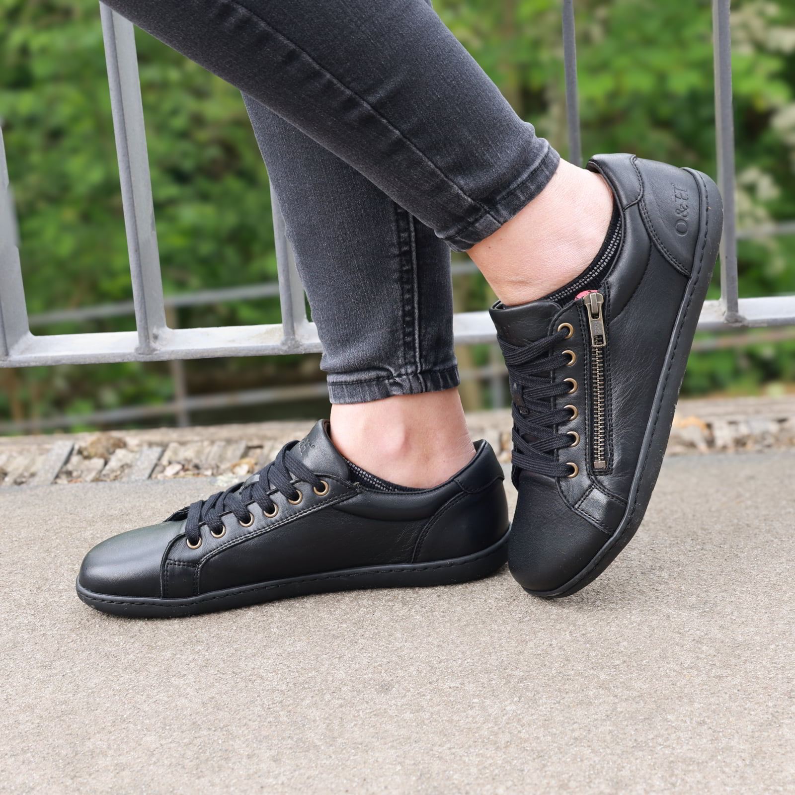 model standing outdoors wearing hazel zip barefoot trainers in black