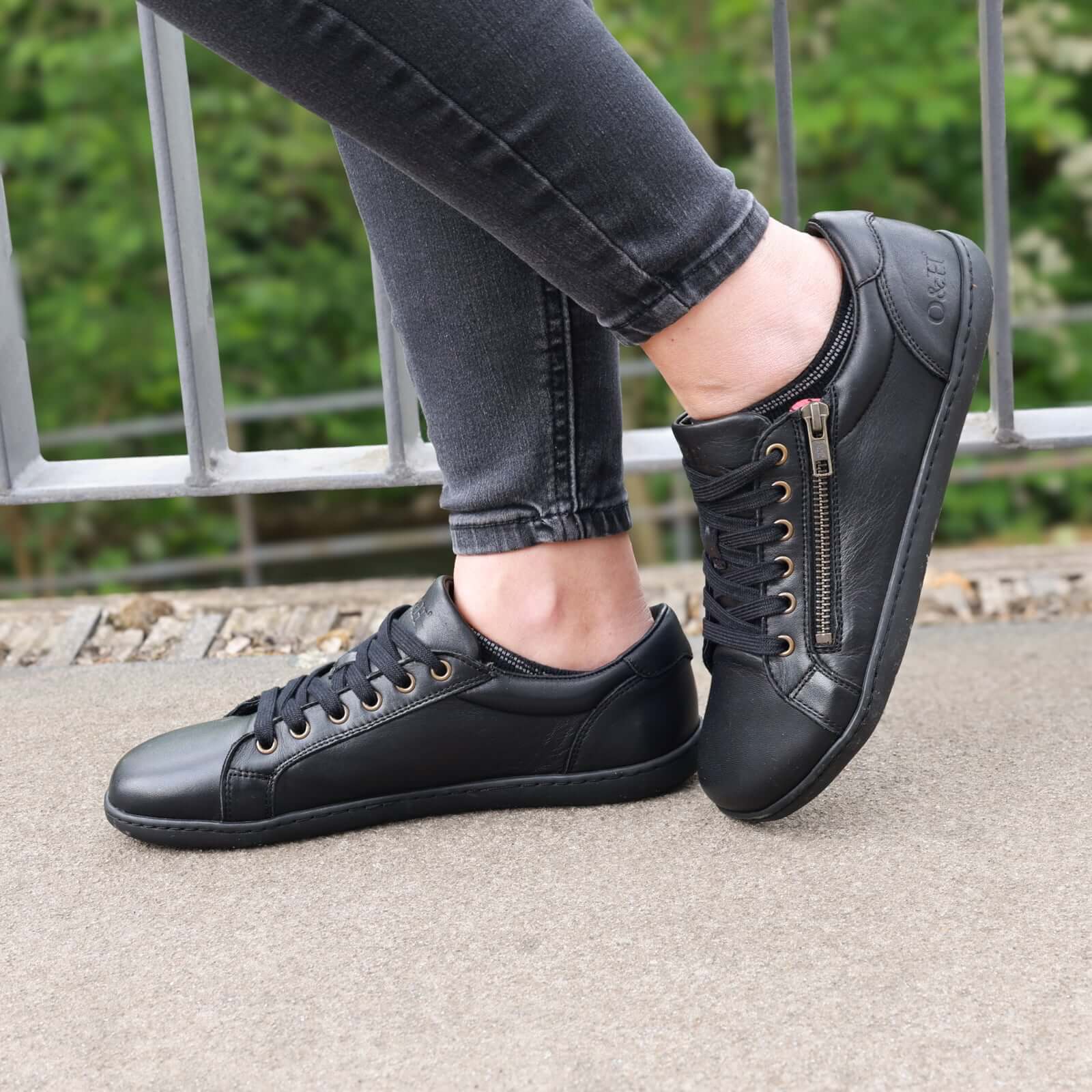 model standing outdoors wearing hazel zip barefoot trainers in black