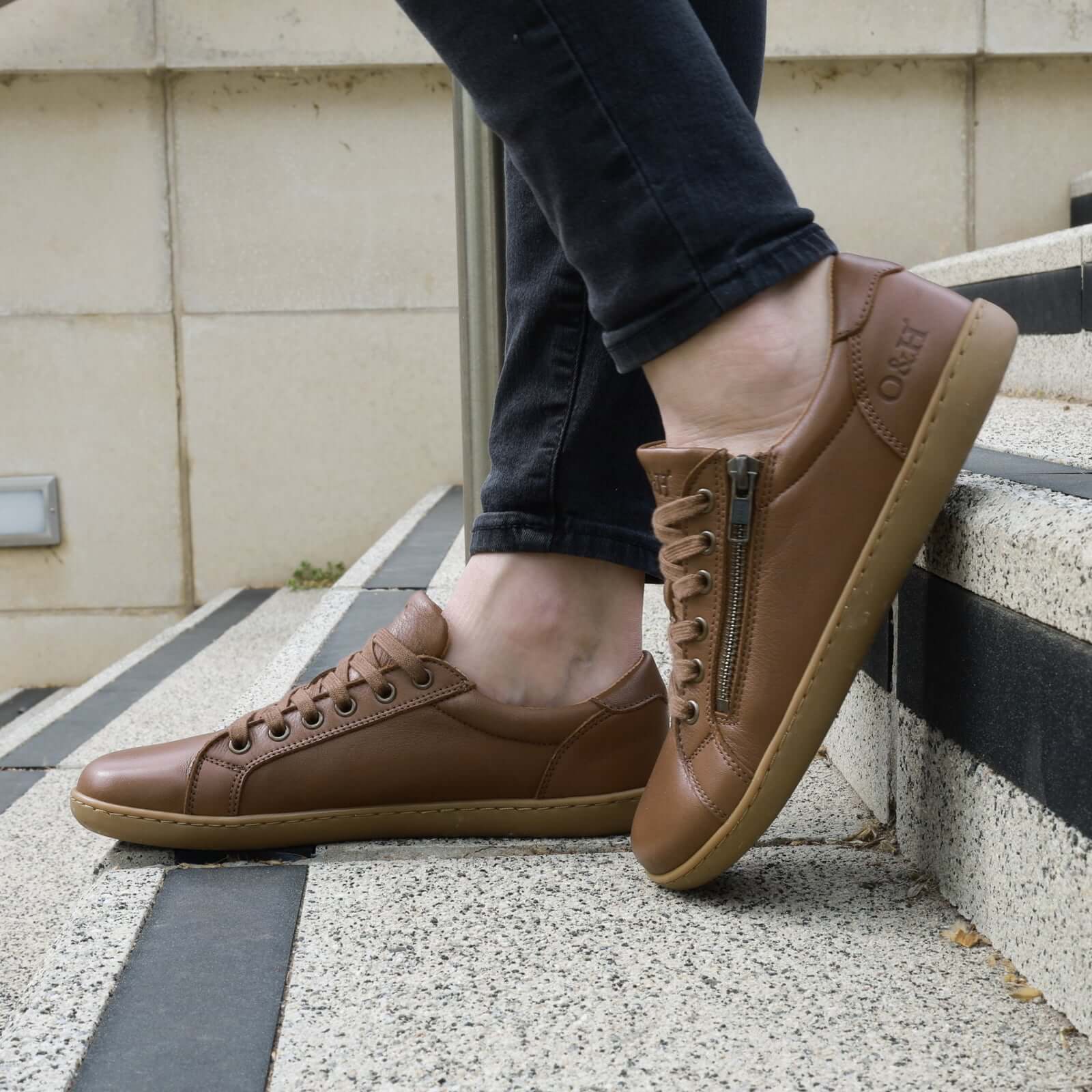 model on steps in the hazel zip barefoot shoes in tan wearing them with dark jeans