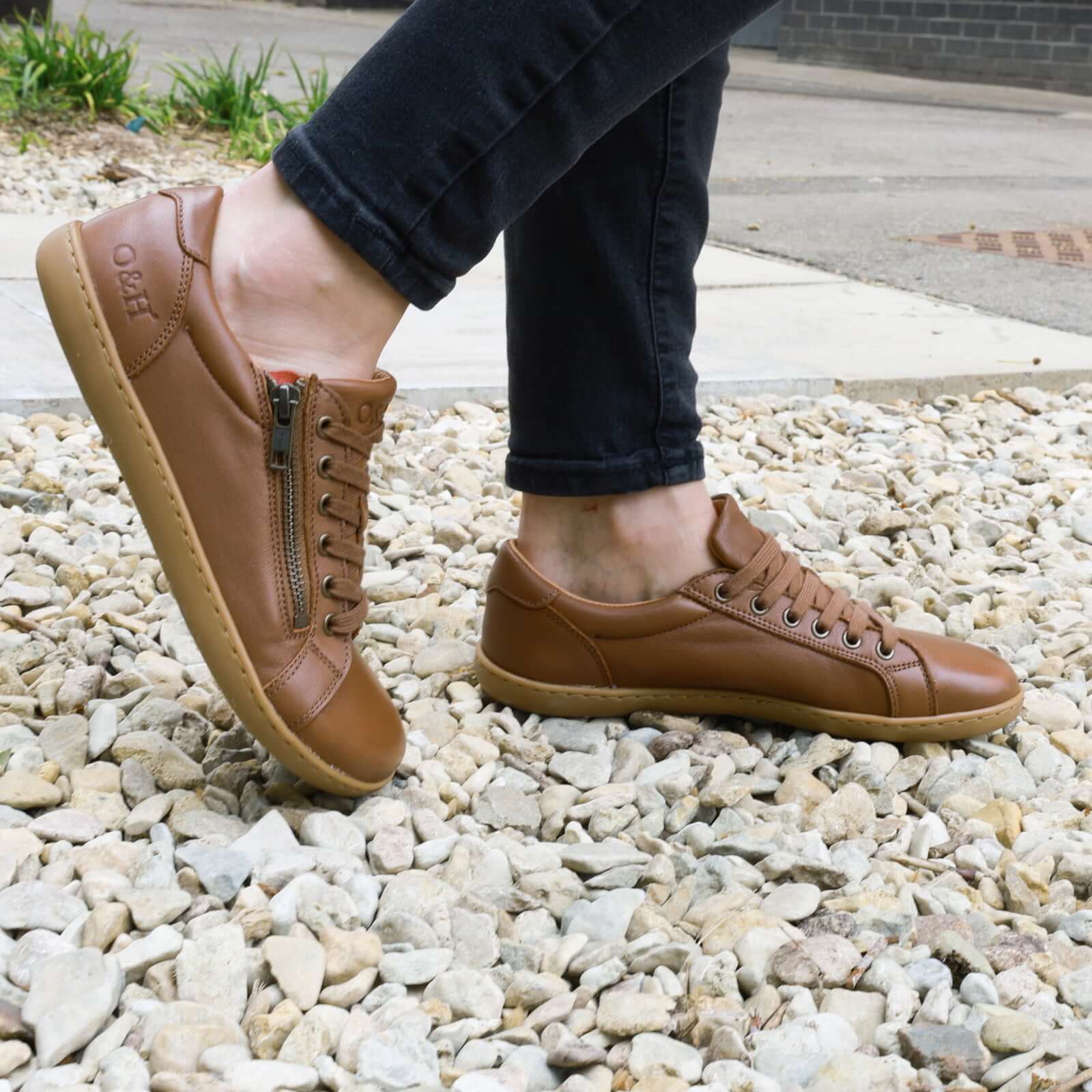 model wearing hazel zip tan barefoot trainers on gravel outdoors