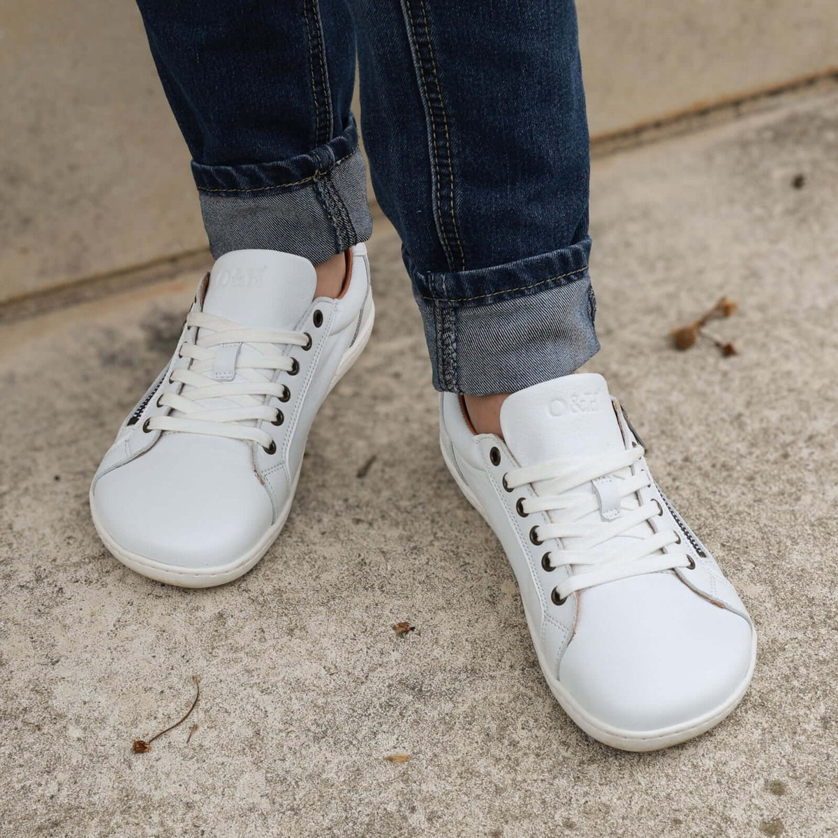 model standing outdoors in hazel zip barefoot trainers in white showing front laces