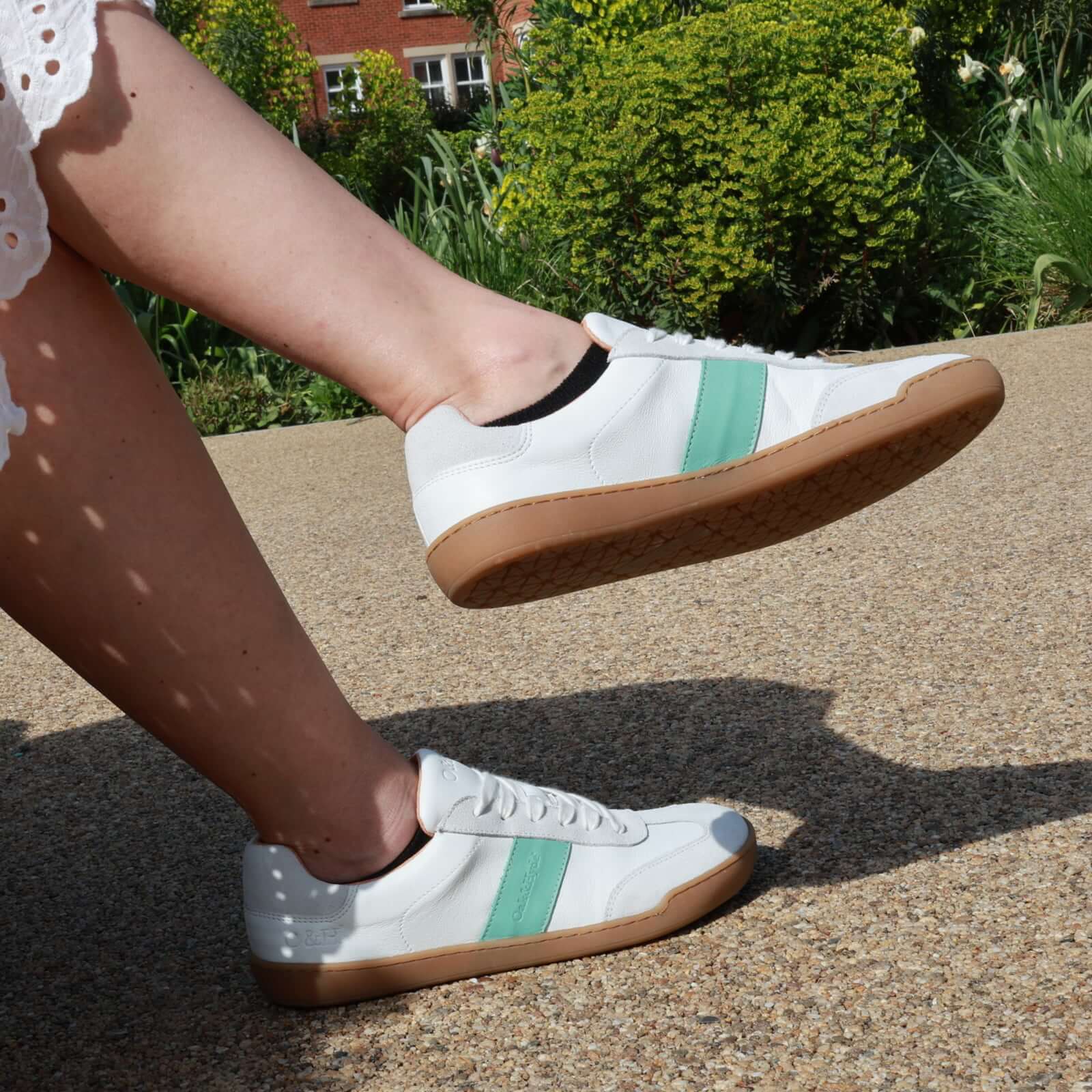 person sitting on a bench wearing white green juniper barefoot trainers
