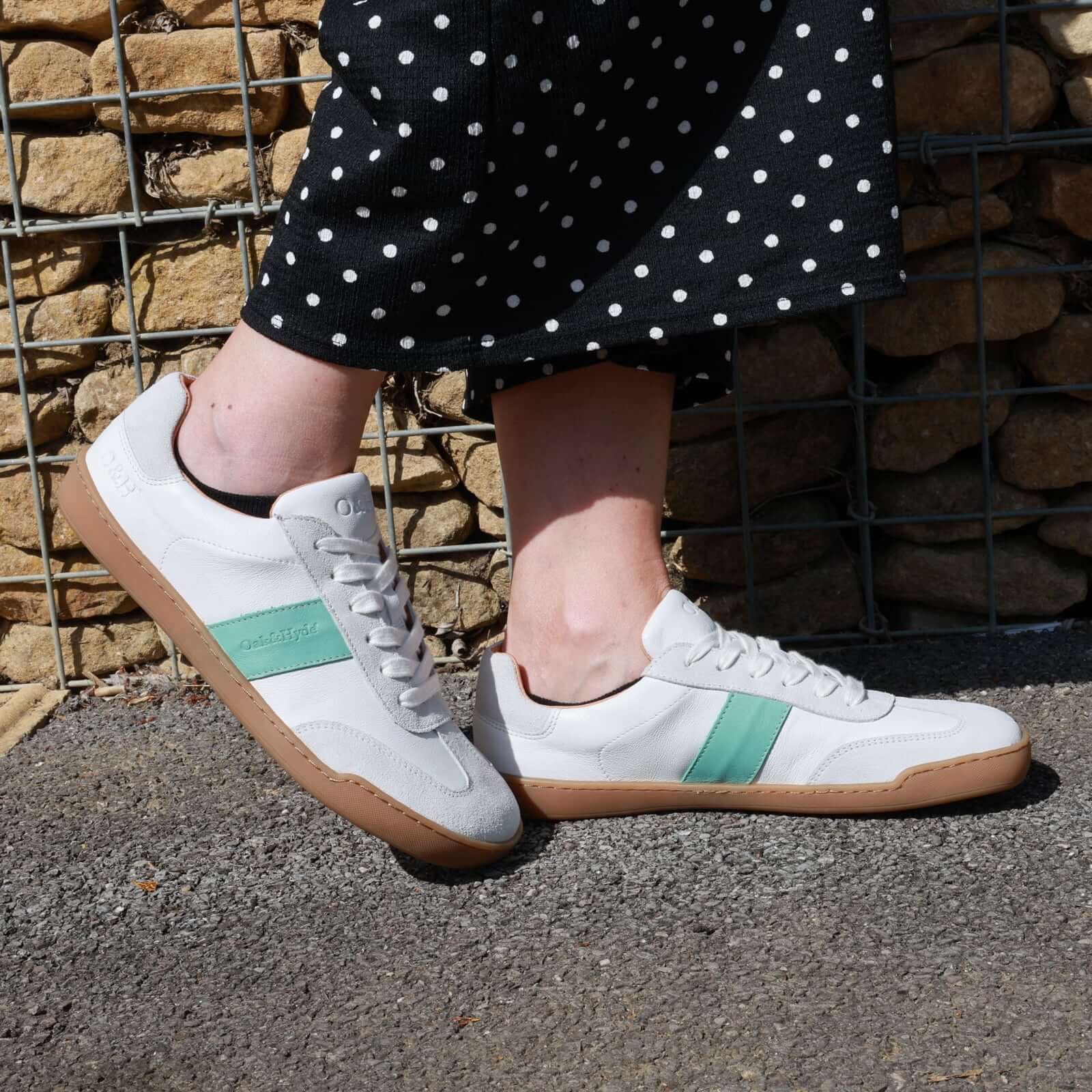 model wearing white green juniper trainers with a black spotty trousers on a pavement