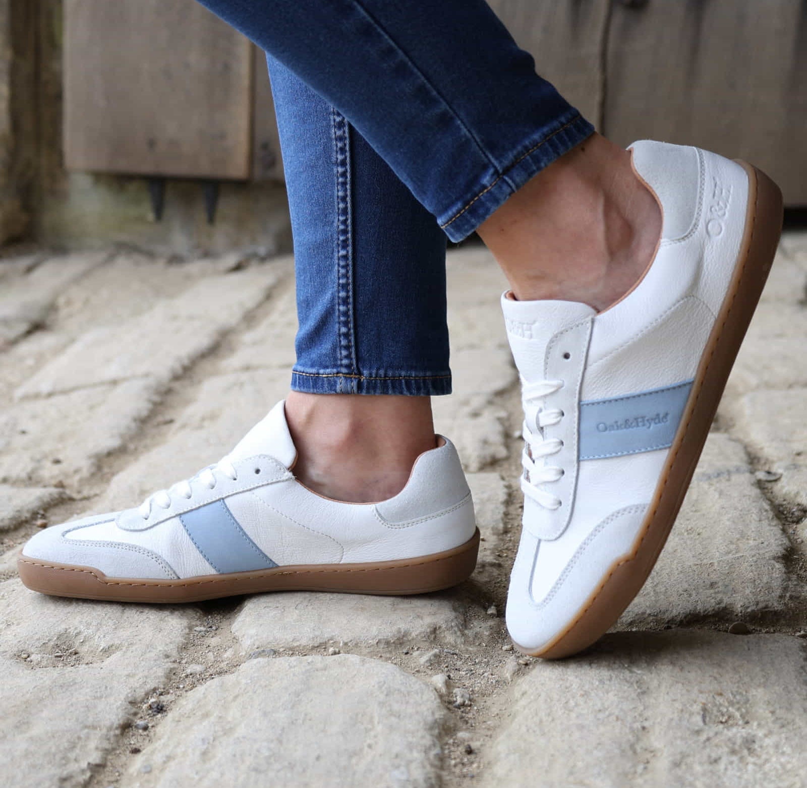 model wearing white barefoot trainers with blue jeans on a stone pavement