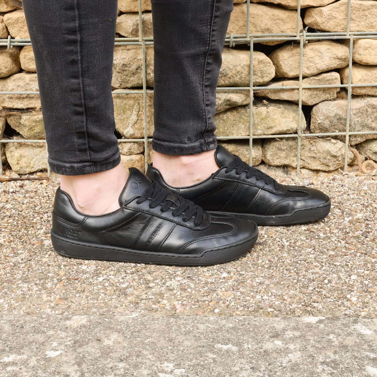 model standing outdoors in the juniper barefoot trainers in all black