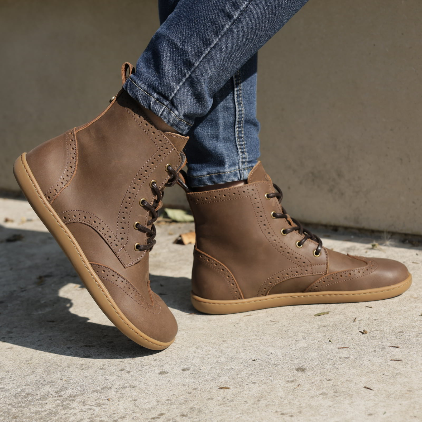 model wearing maple mid barefoot brogue boots in brown with blue jeans outdoors