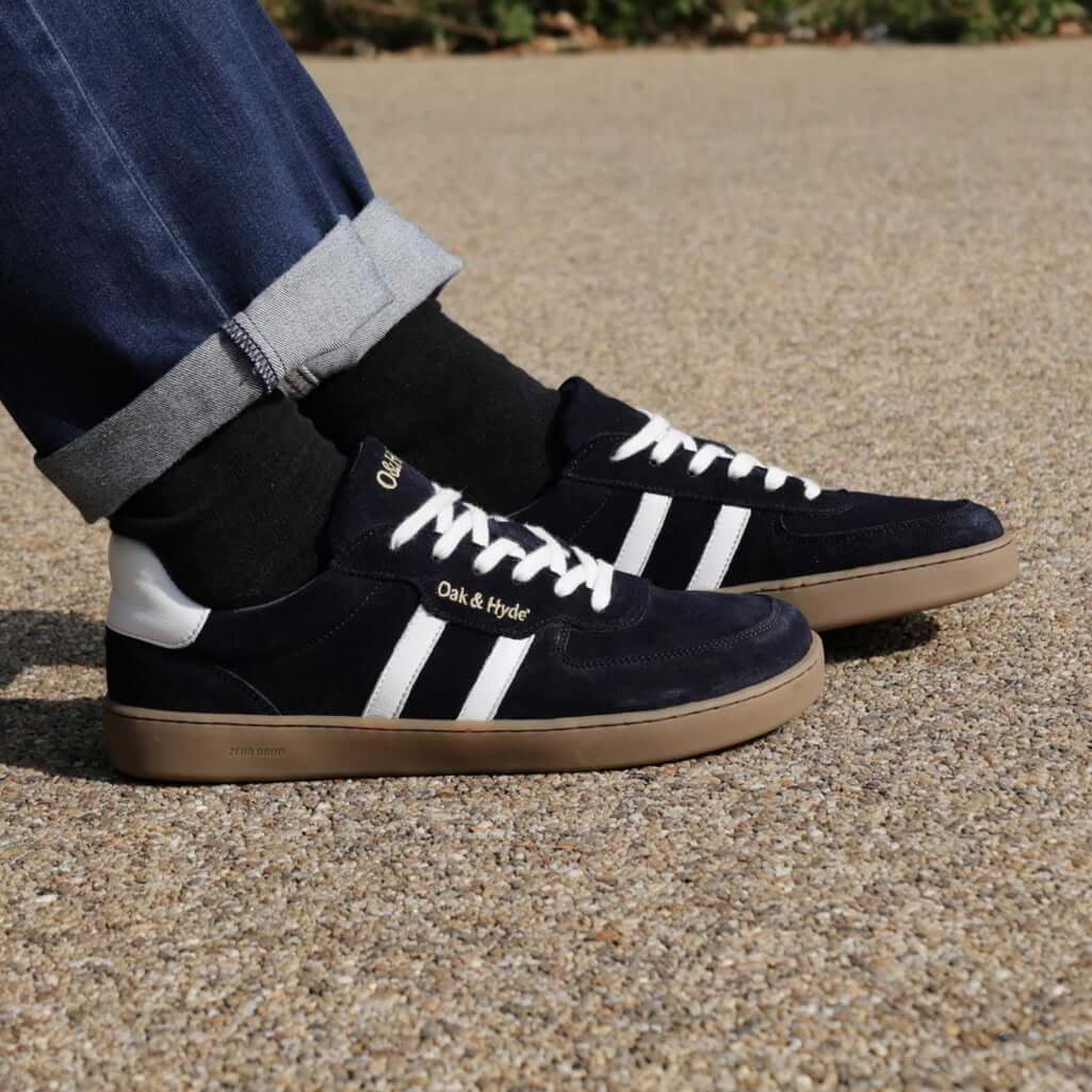 person wearing mens larch barefoot trainers in navy with blue jeans sat on bench