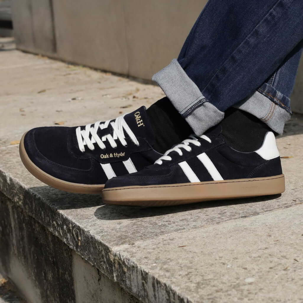 model sat on stone step wearing mens larch barefoot trainers in navy with blue jeans