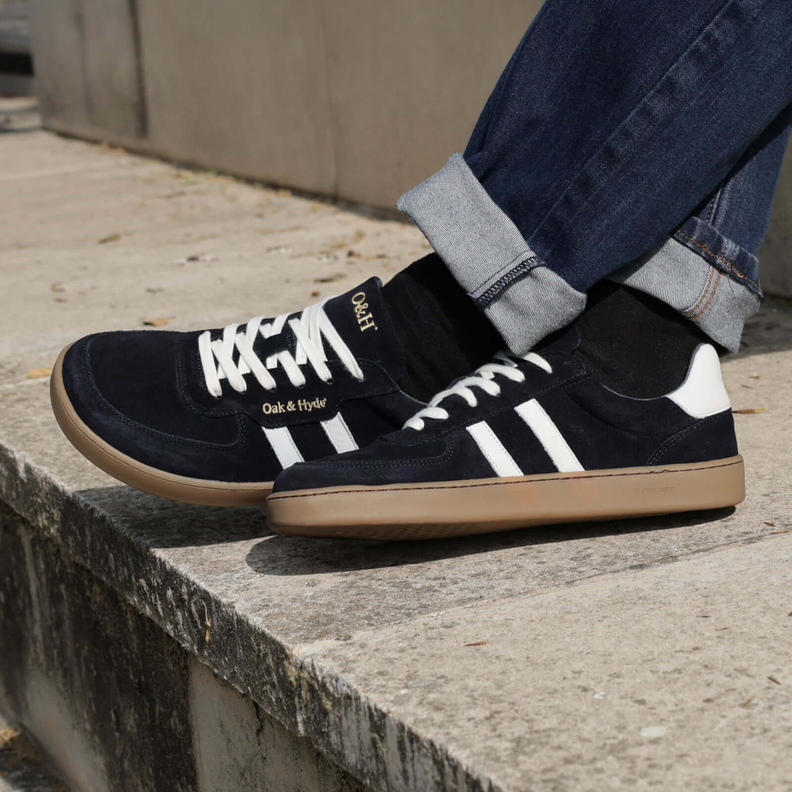 model sat on stone step wearing mens larch barefoot trainers in navy with blue jeans