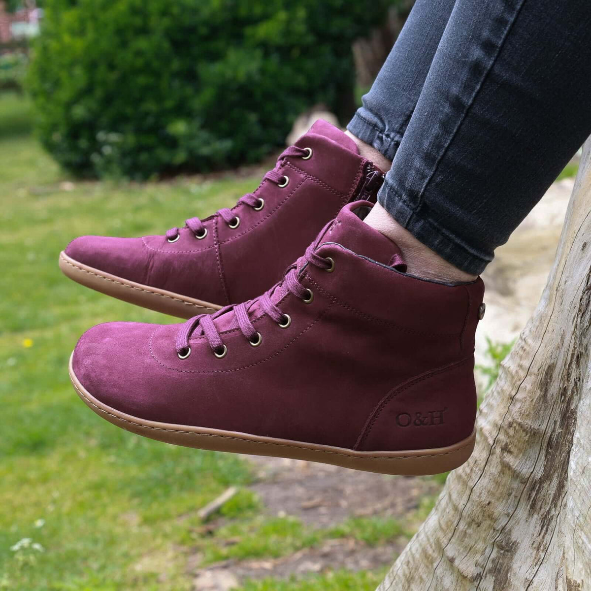 model sitting on tree trunk wearing mulberry barefoot ankle boots in wine with jeans