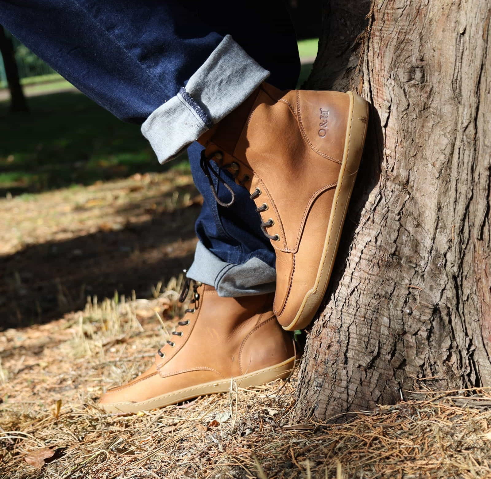 model wearing redwood barefoot boots with blue jeans rolled up leaning against a tree