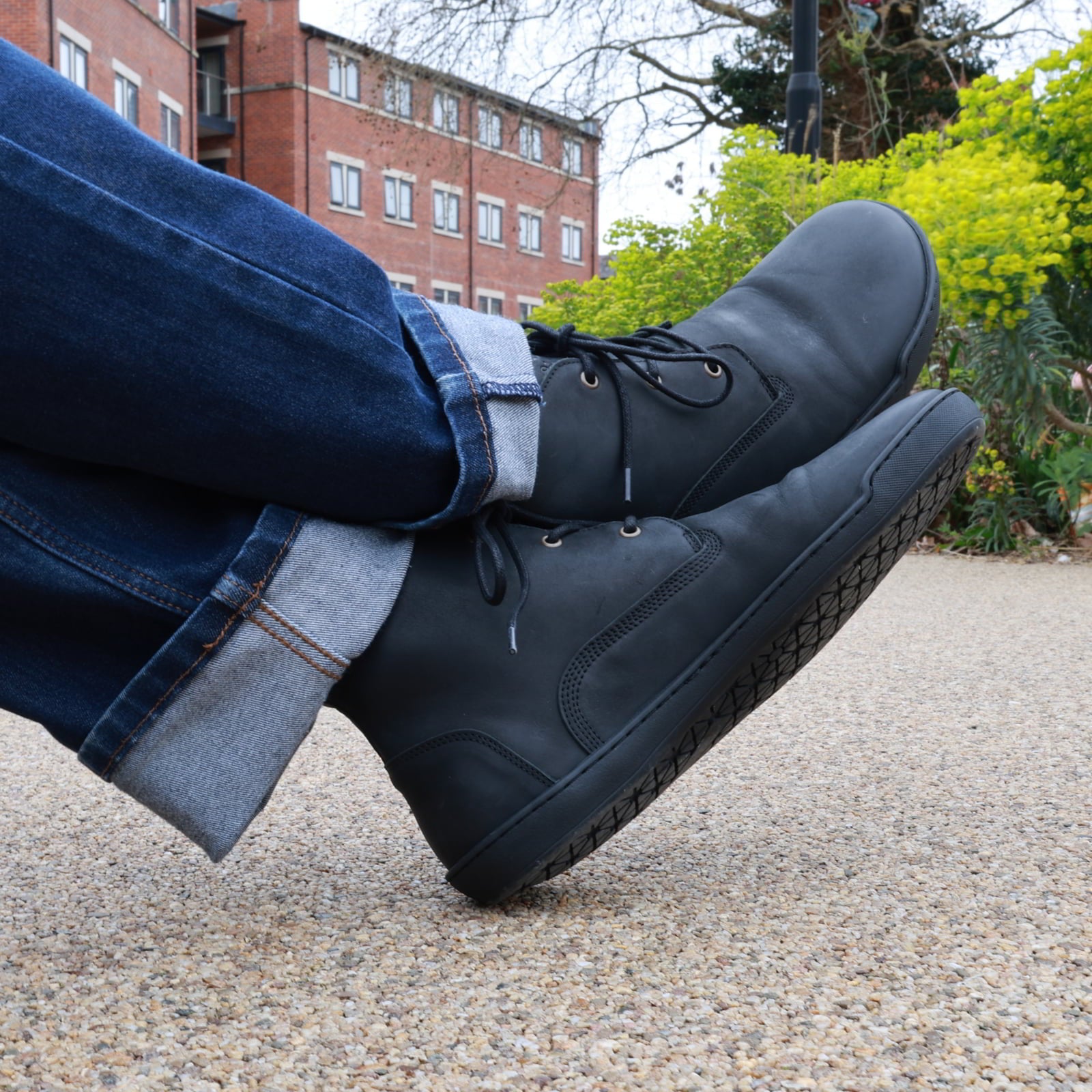 person wearing black spruce barefoot chukka boots sitting on a bench outdoors