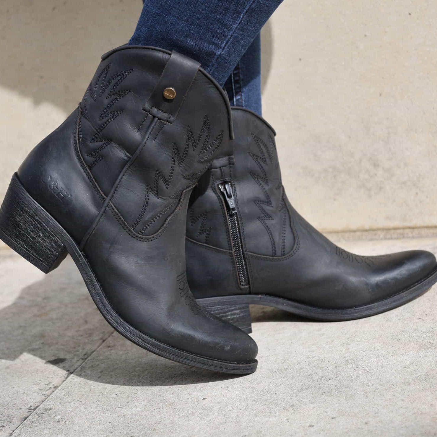 model wearing black cowboy boots with blue jeans on concrete