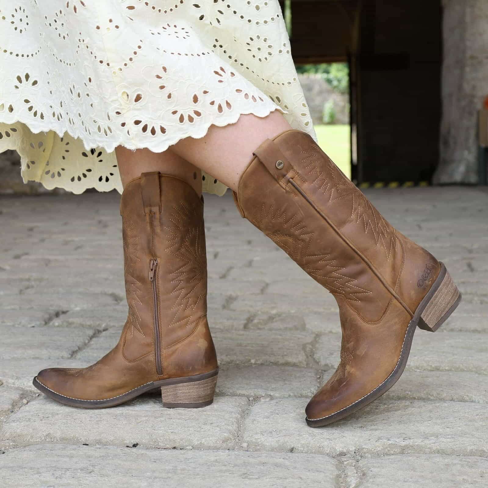 Brown knee-high boots worn with a yellow lace dress on a stone pavement