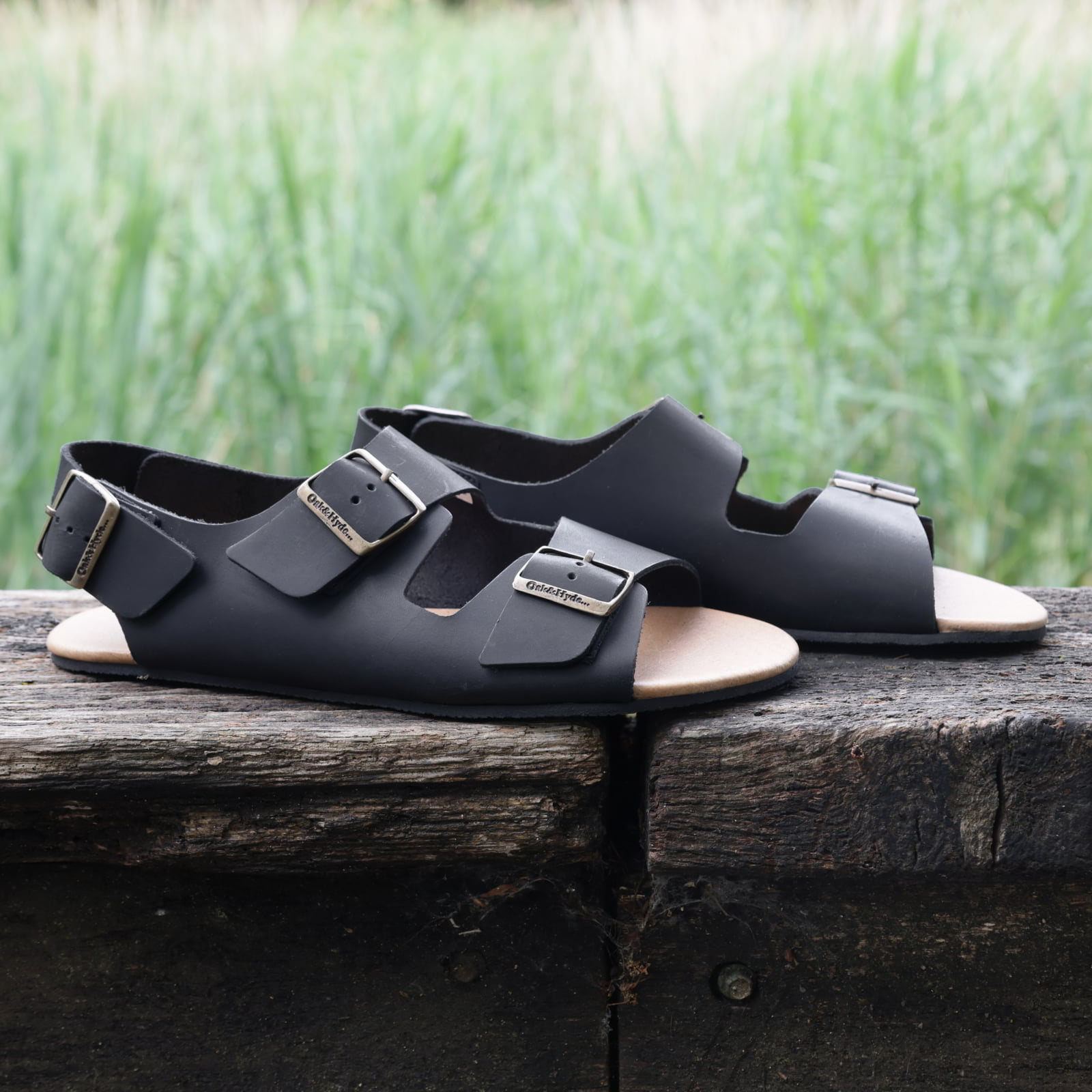 pair of wisteria barefoot sandals in black on a wooden beam showing leather upper