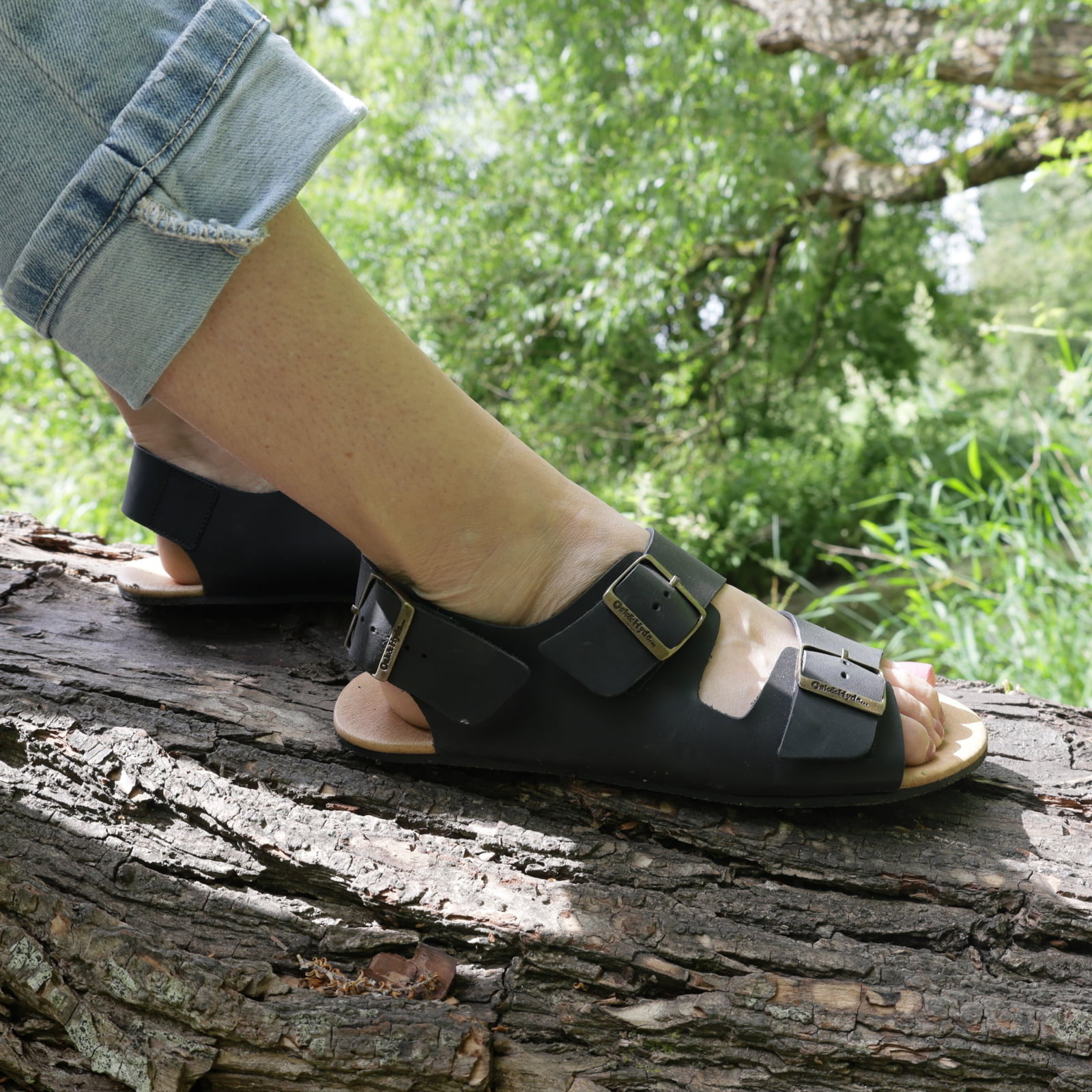 model wearing wisteria barefoot sandals in black with blue jeans sitting on a tree branch