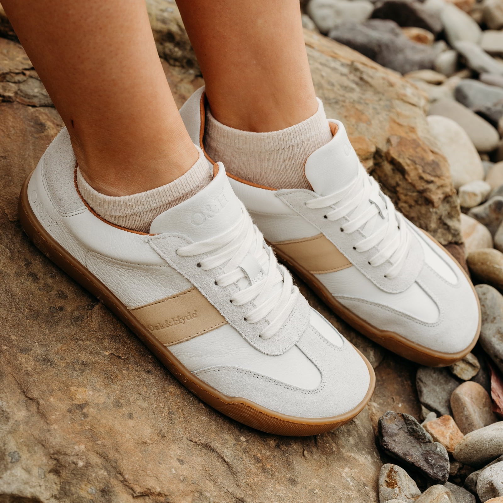 model sitting on rock wearing juniper white beige barefoot trainers