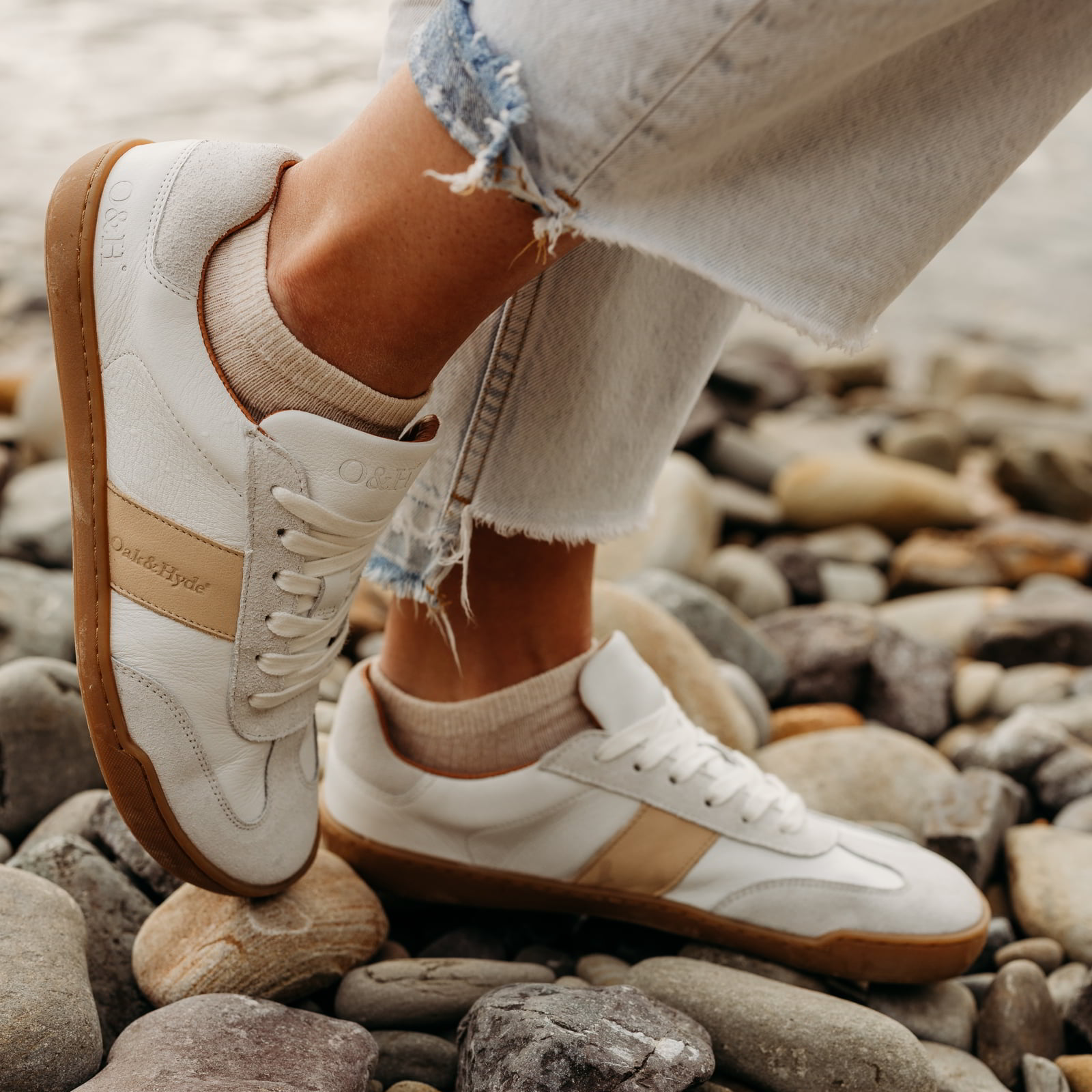 model standing on pebbled beach wearing juniper white beige barefoot trainers