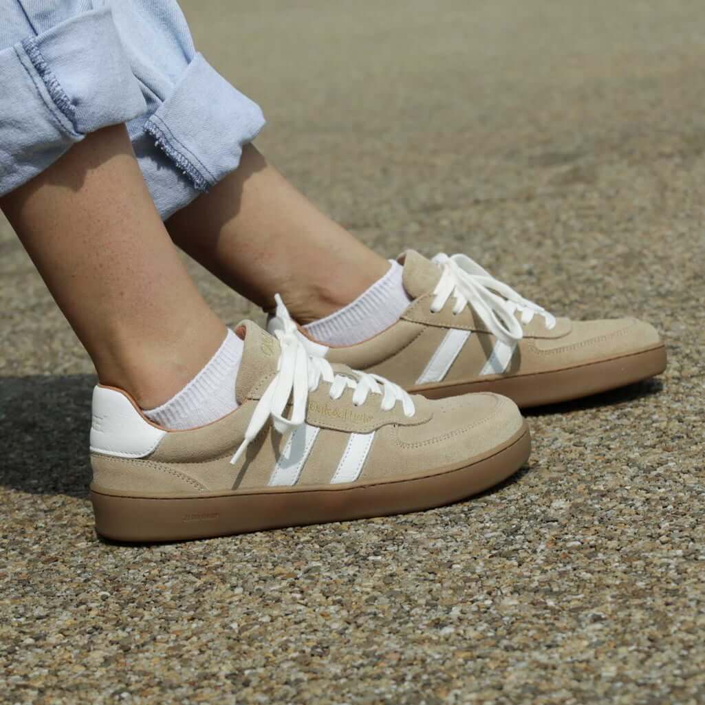 person wearing womens larch barefoot trainers in beige sitting on a bench outdoors