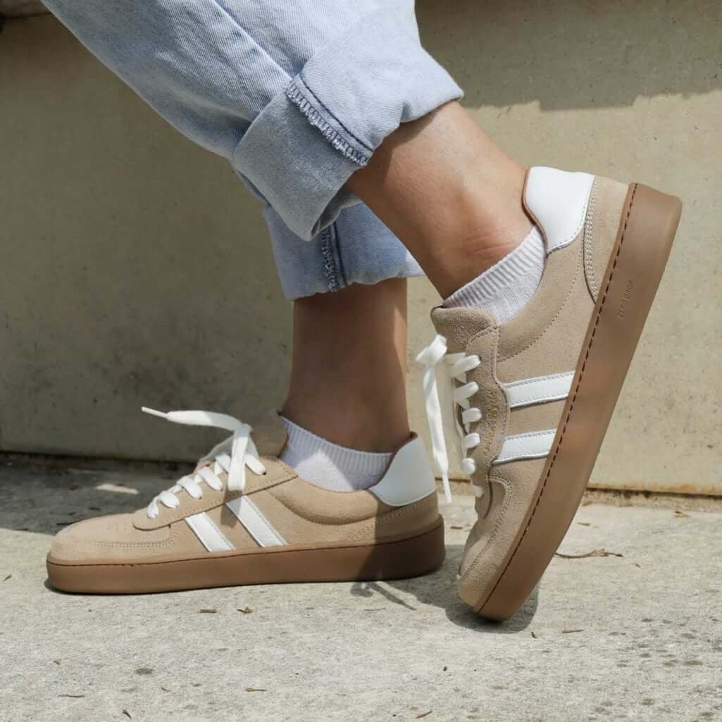 model standing outdoors wearing womens larch barefoot trainers in beige with blue jeans