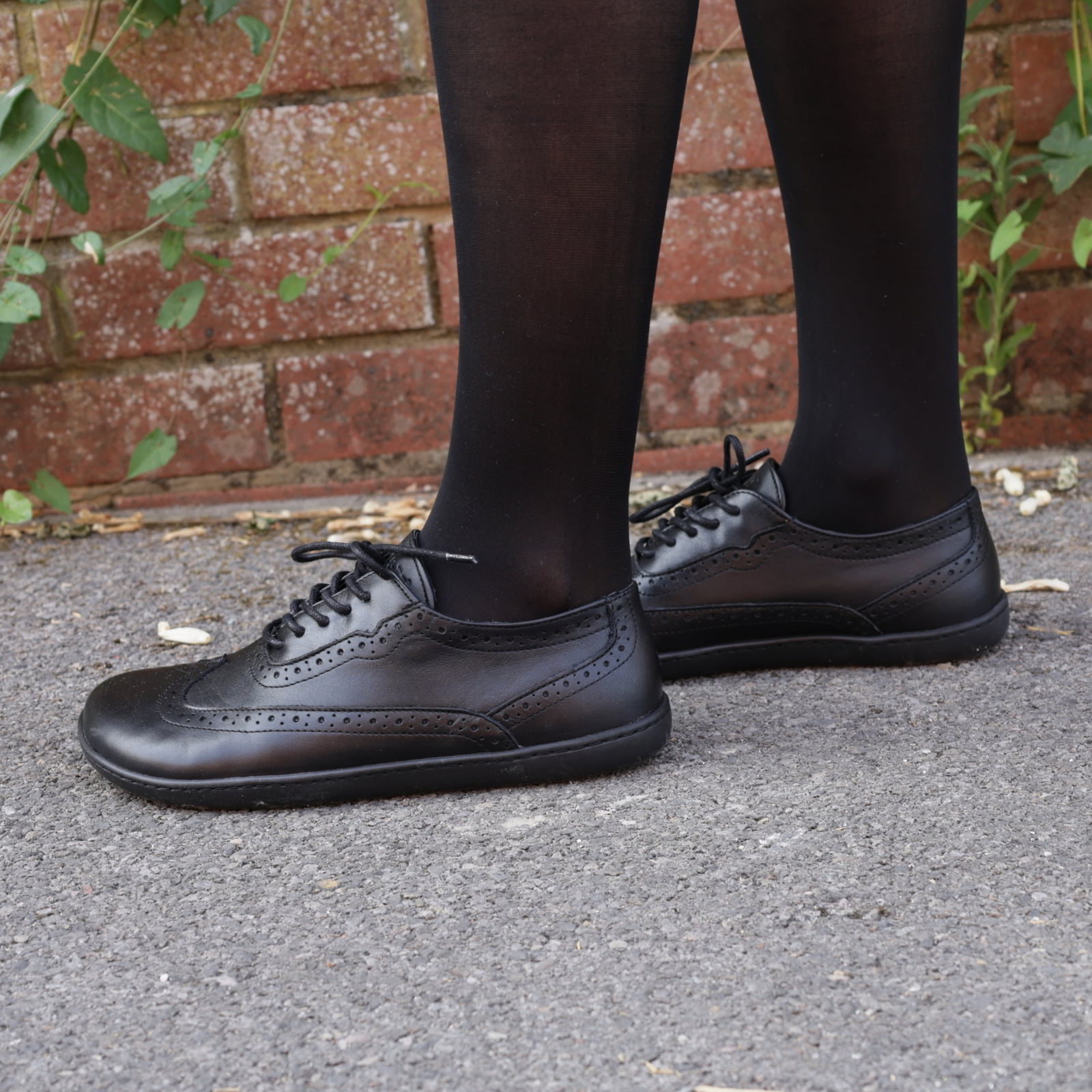 model standing on pavement in black maple brogue barefoot shoes worn with black tights